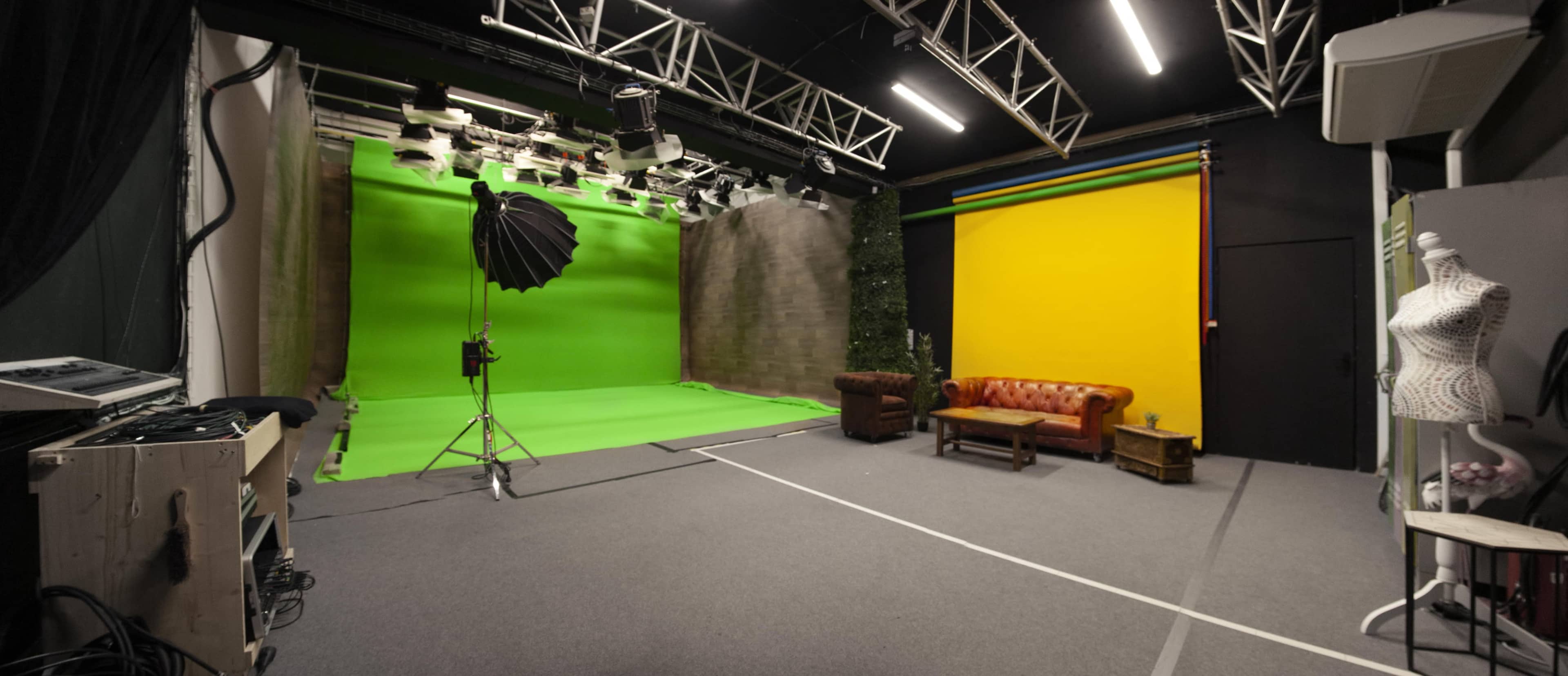 The image shows a photography studio featuring a green screen, a yellow backdrop, a vintage sofa, and professional lighting equipment.