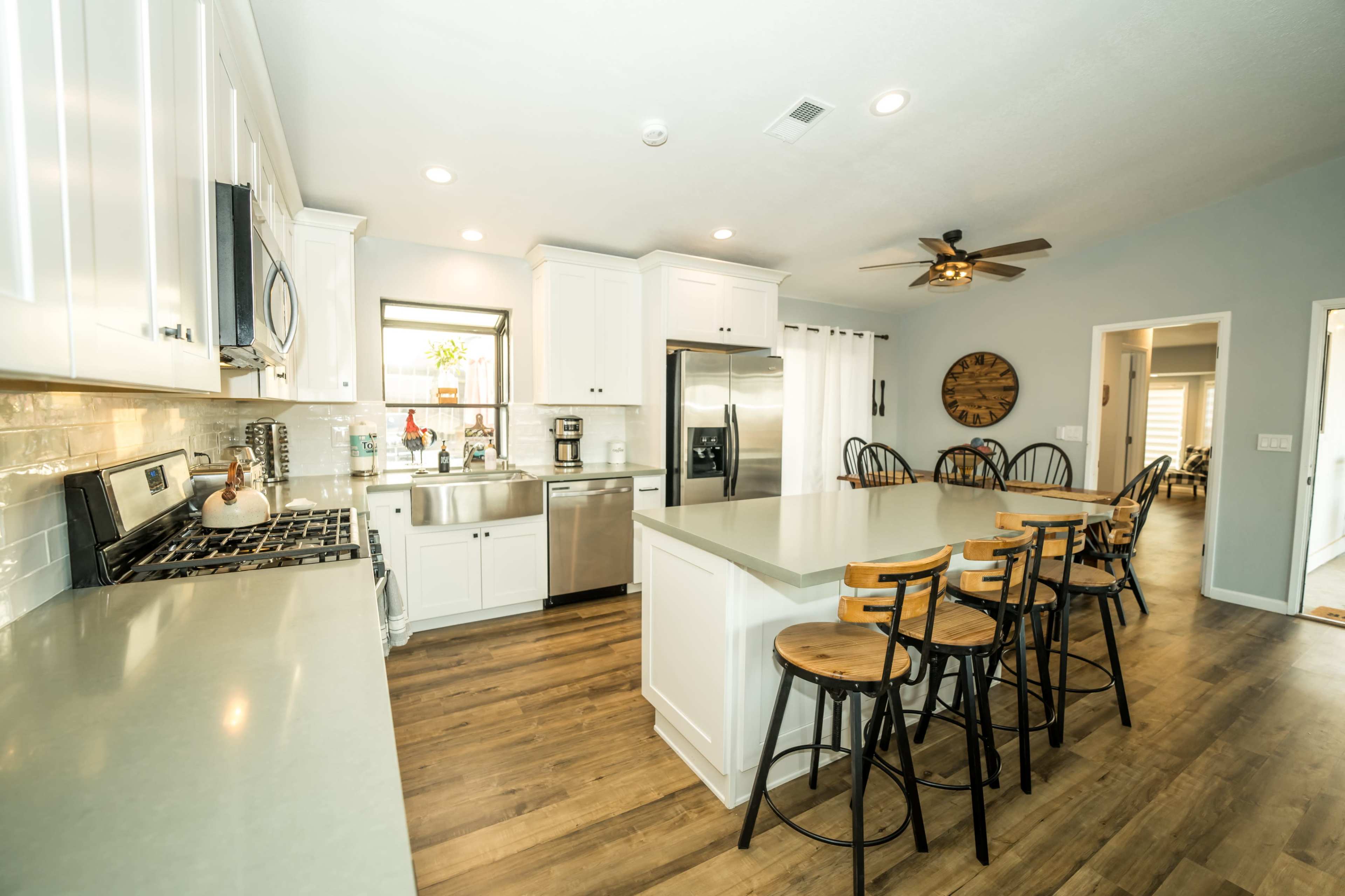 A modern kitchen features white cabinetry, stainless steel appliances, and a central island with barstools, complemented by wood flooring.