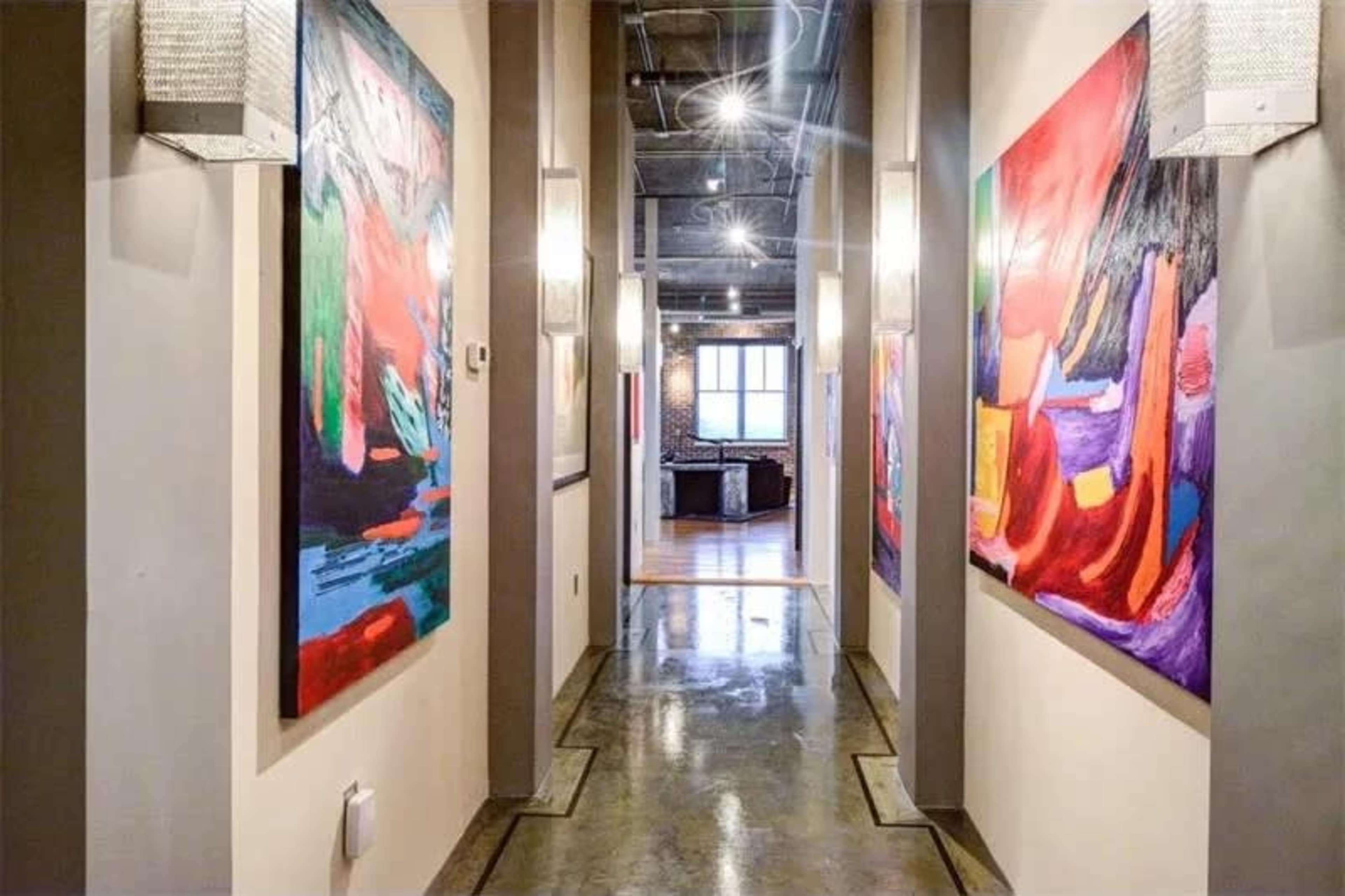 A narrow hallway displays brightly colored abstract paintings on the walls, leading to a room at the end.