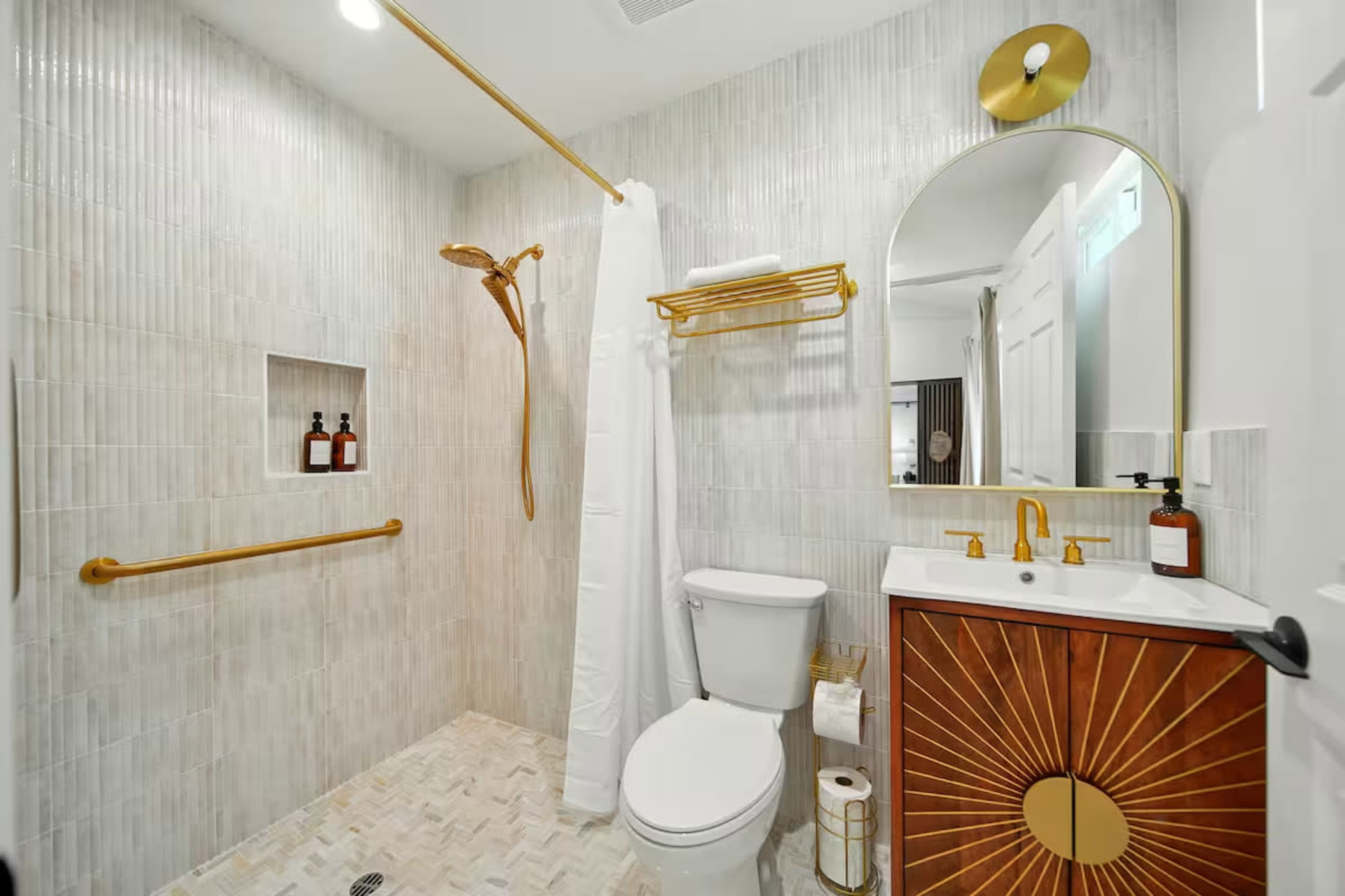The image shows a modern bathroom with a shower, toilet, and a vanity featuring a round mirror and decorative wall tiles.