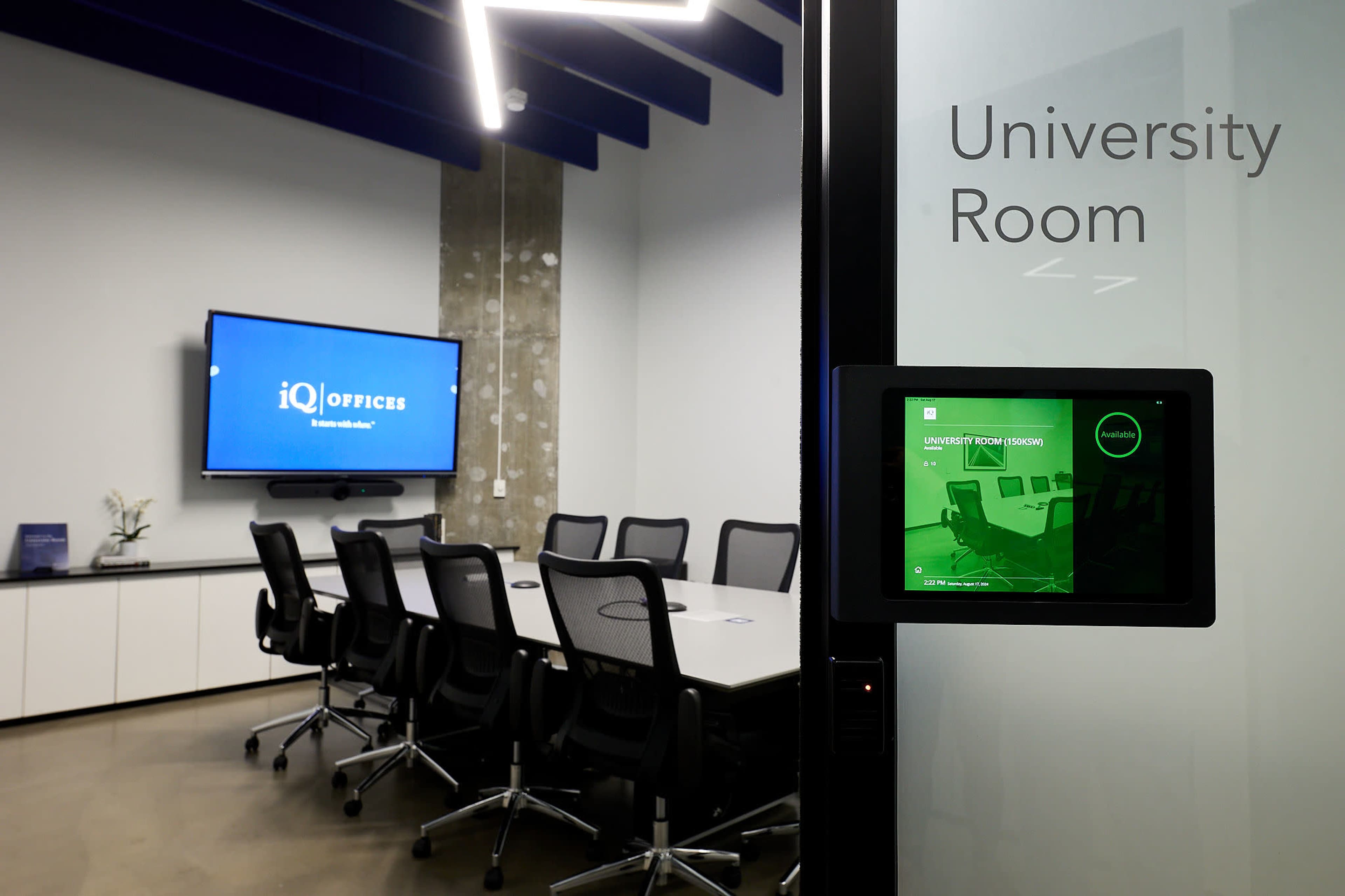 The image shows a conference room labeled "University Room," featuring a large screen and a long table surrounded by chairs.
