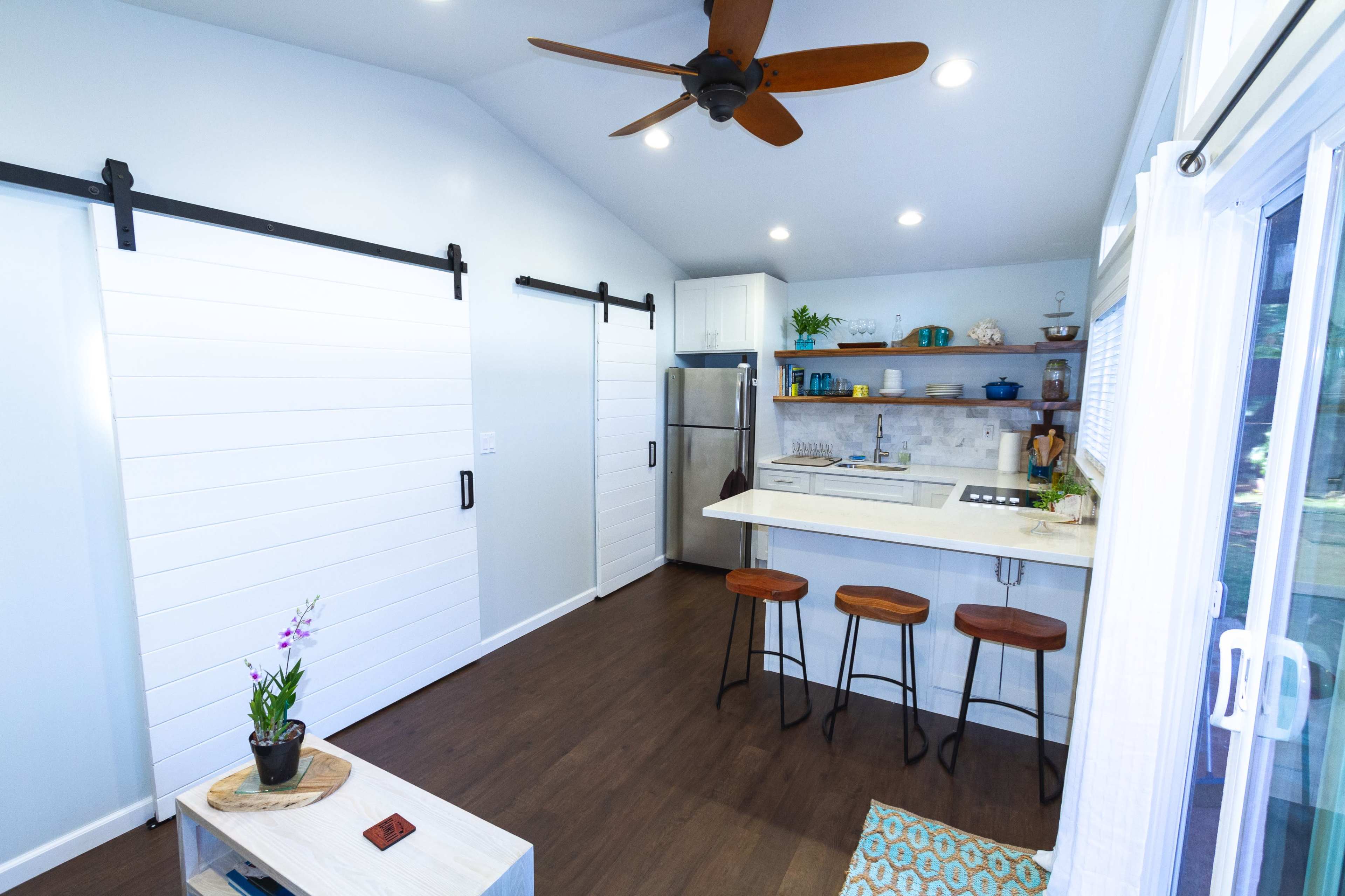 A modern kitchen with a bar area, three stools, white sliding barn doors, and a light blue wall.