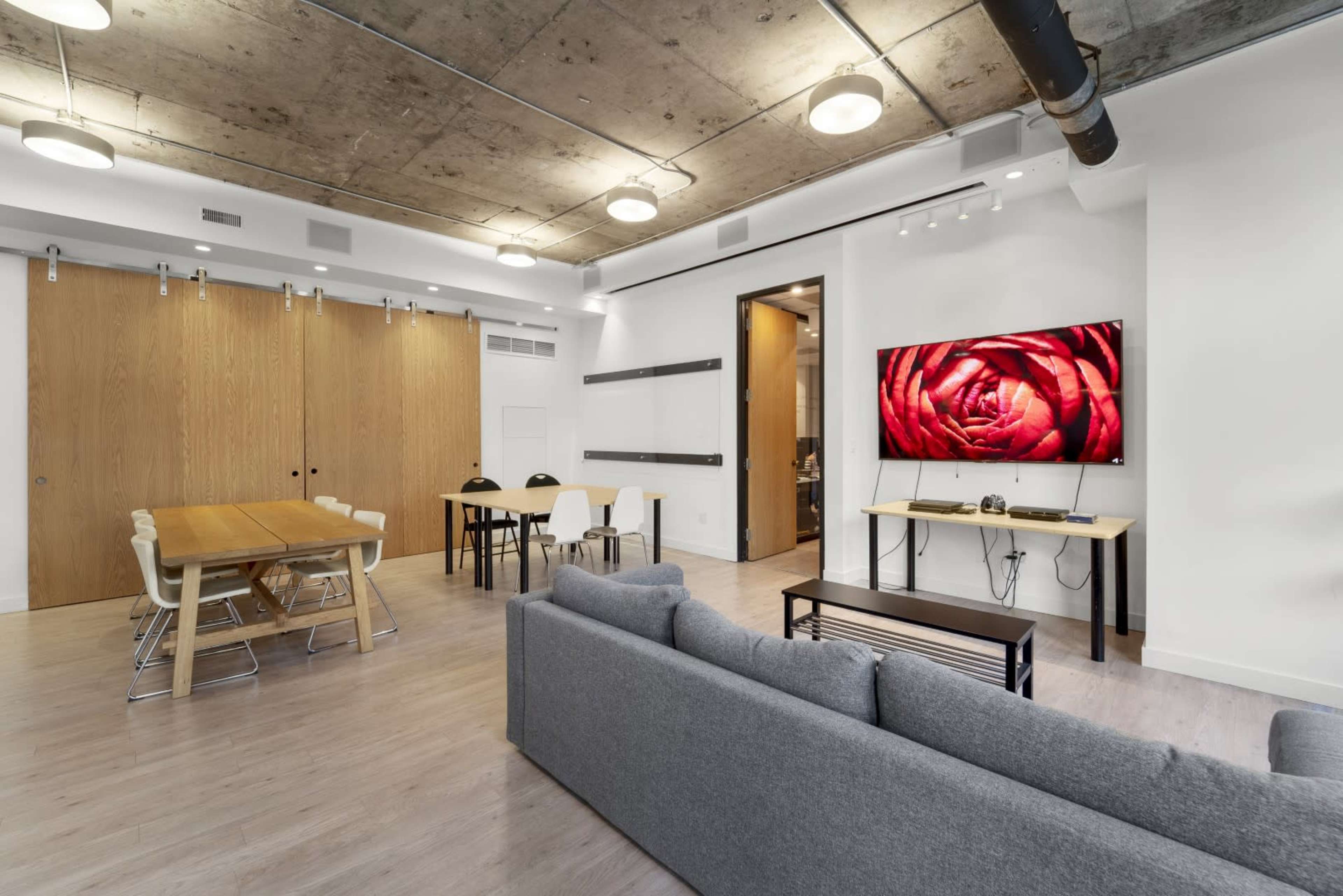 A modern living space featuring a gray sofa, a wooden dining table, and a large TV mounted on a wall displaying a close-up of a red rose.