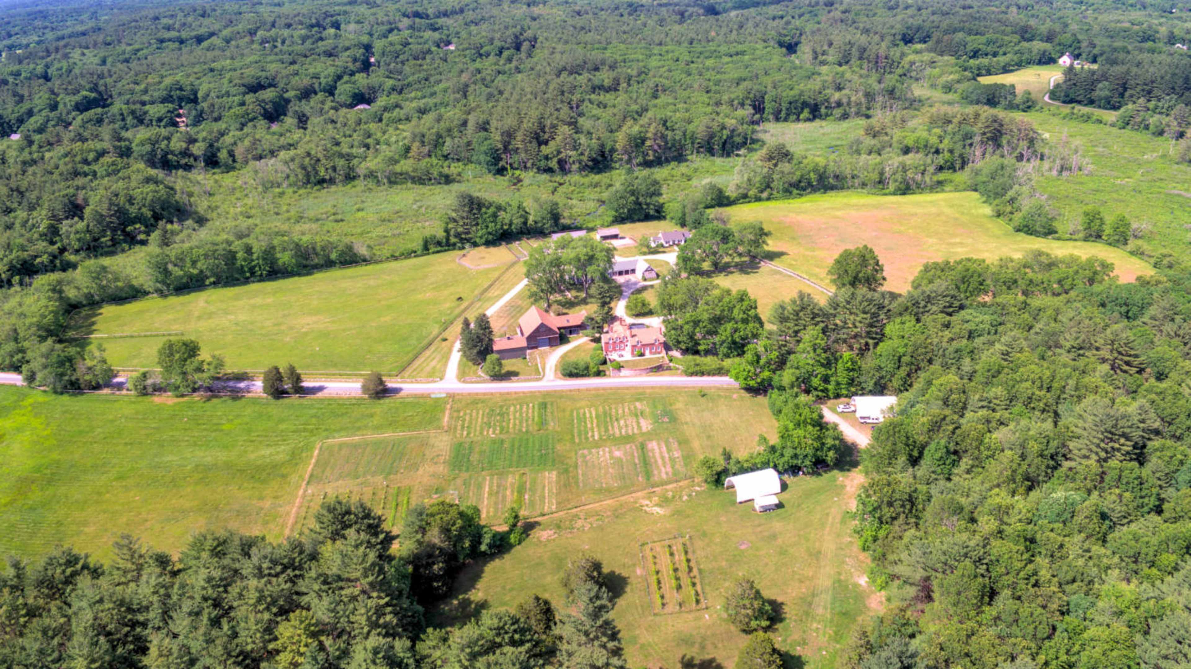 The image shows an aerial view of a large rural property featuring several buildings, fields, and patches of forest.