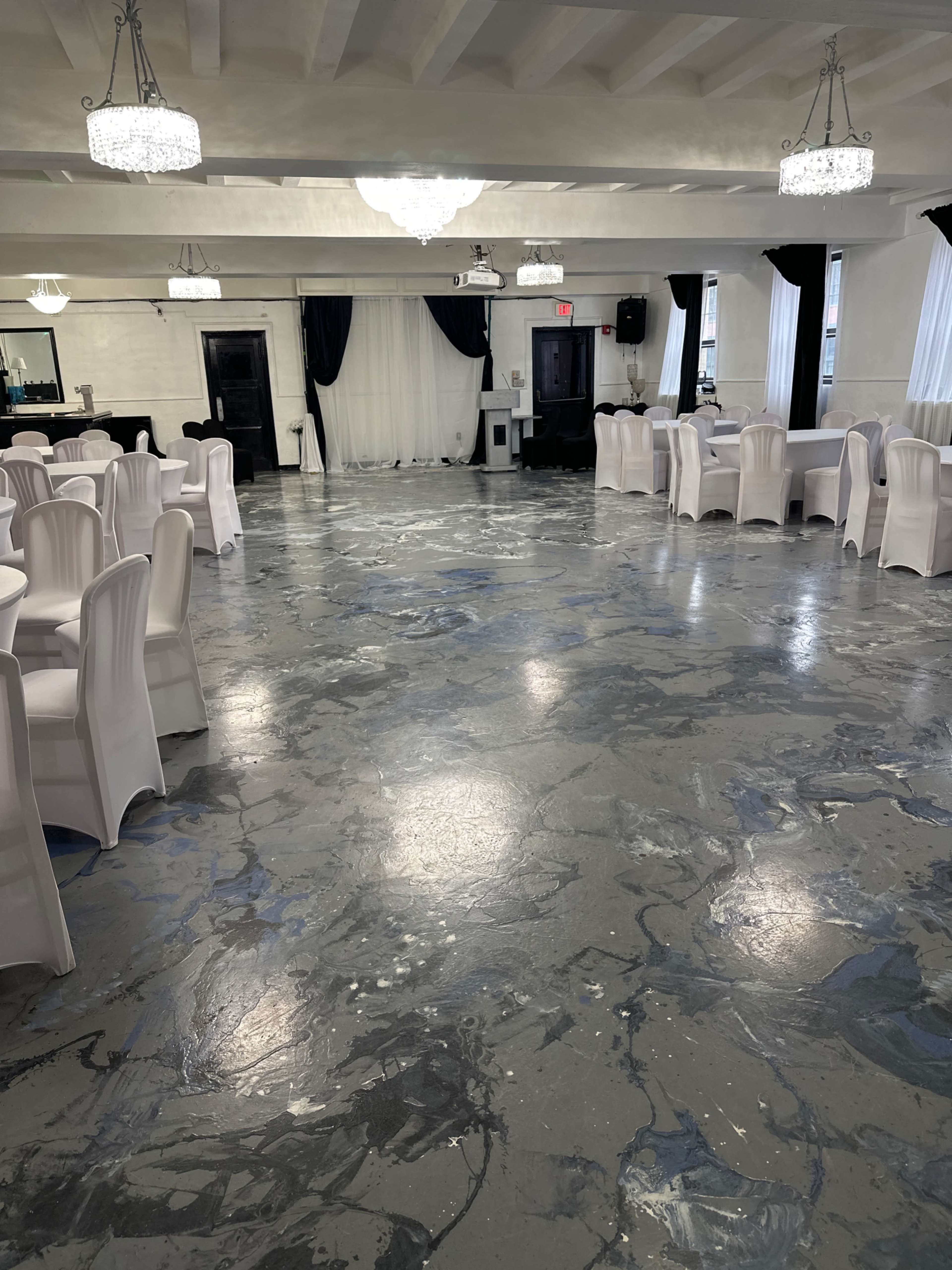 A spacious event hall with gray marbled flooring, white chairs, and chandeliers hanging from the ceiling.