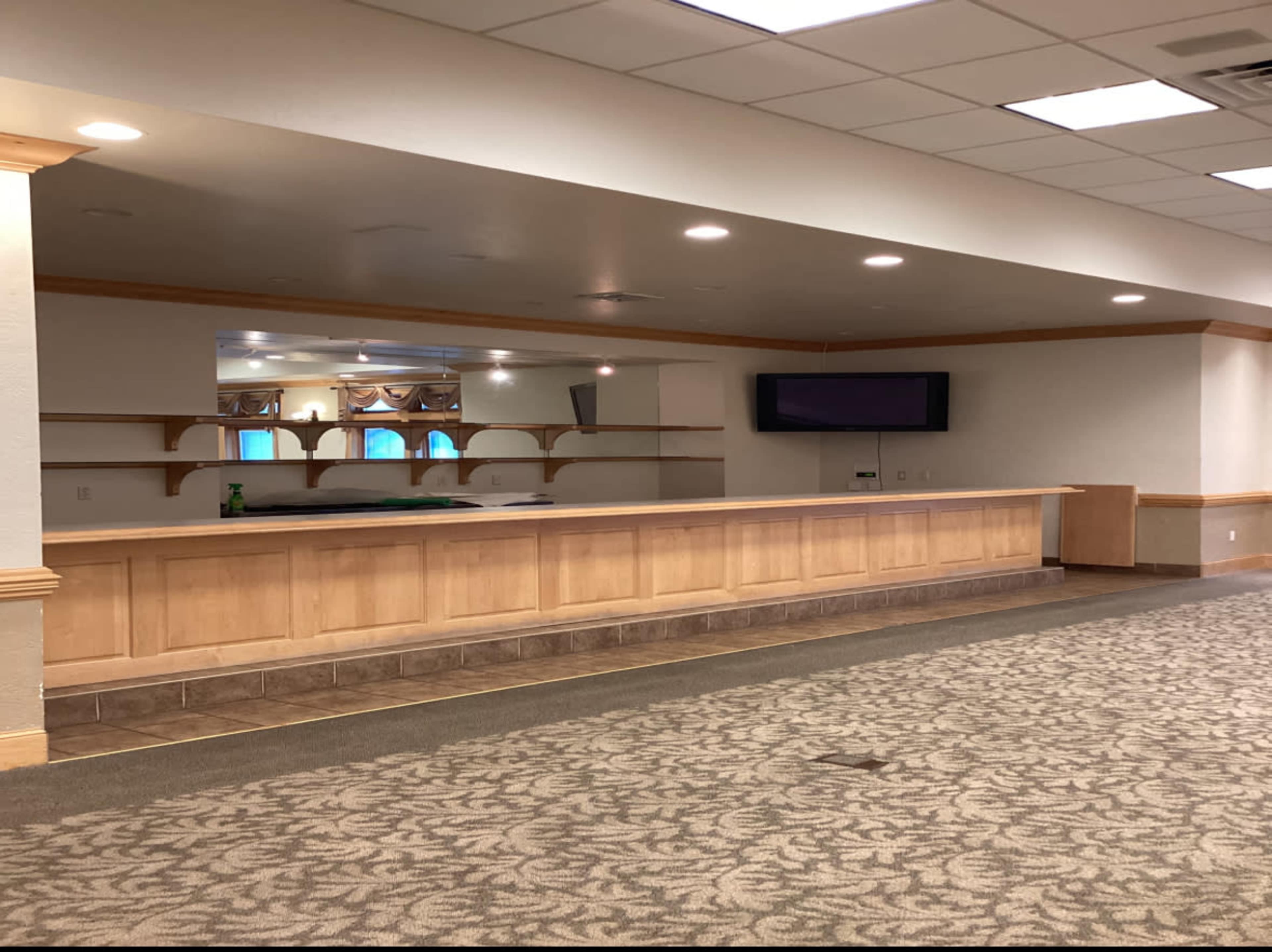 The image shows an empty reception area with a wooden counter, a large mirror, and a television mounted on the wall.