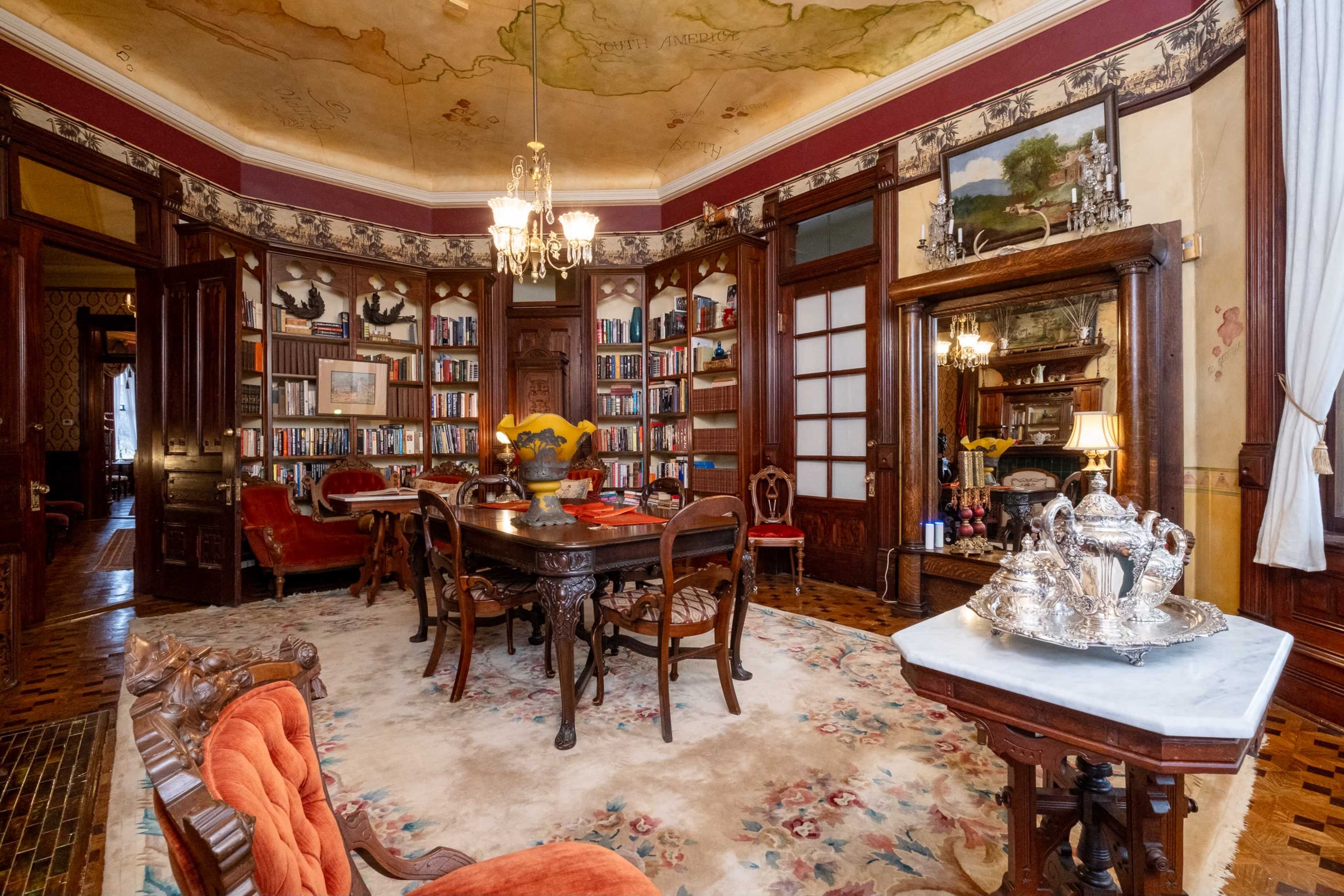 The image shows an ornate room with bookshelves lining the walls, a round table in the center, and decorative furniture, including a silver tea set.