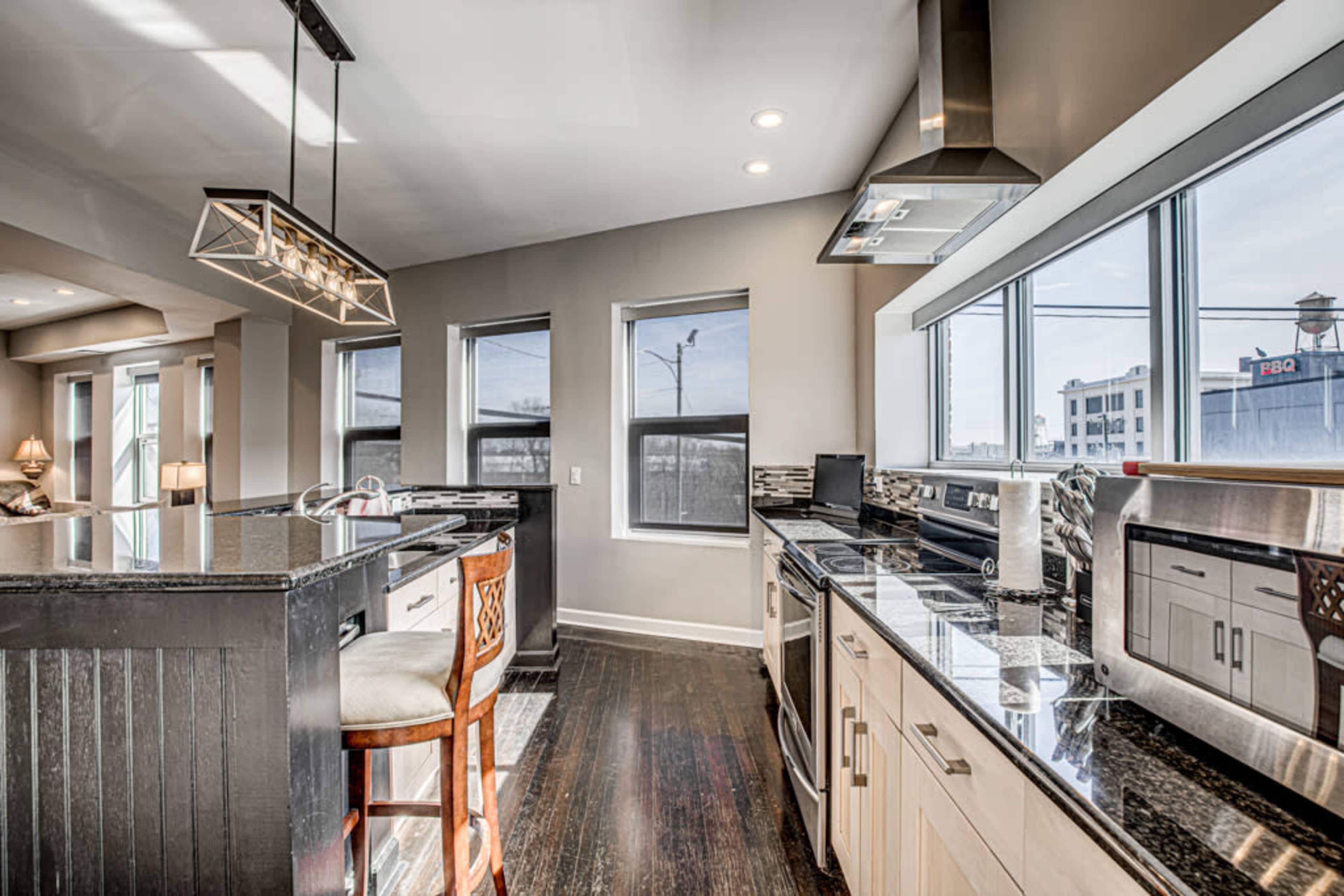 A modern kitchen with granite countertops, stainless steel appliances, and large windows providing natural light.