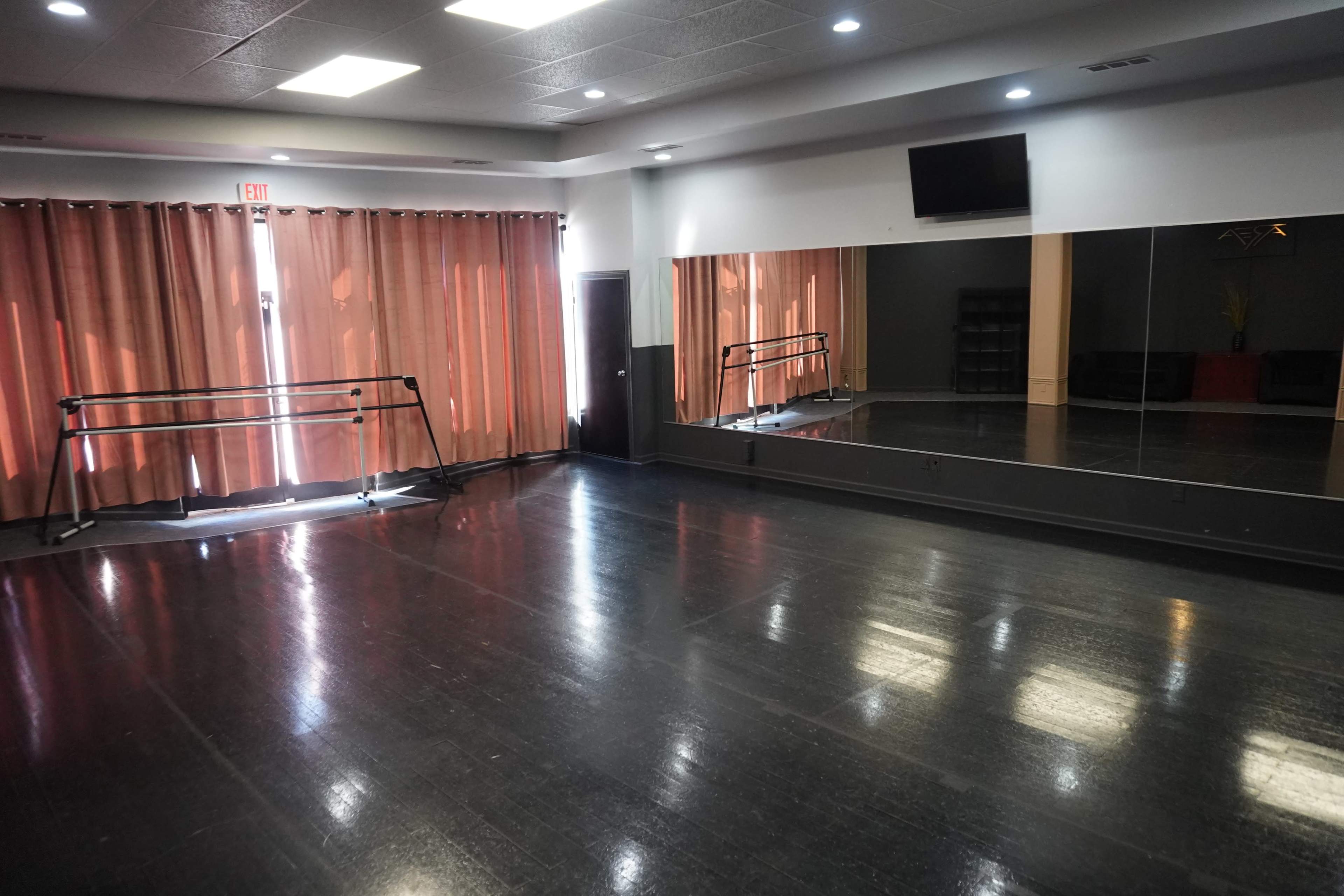 A dance studio with mirrored walls, a barre, and large curtains covering the windows.