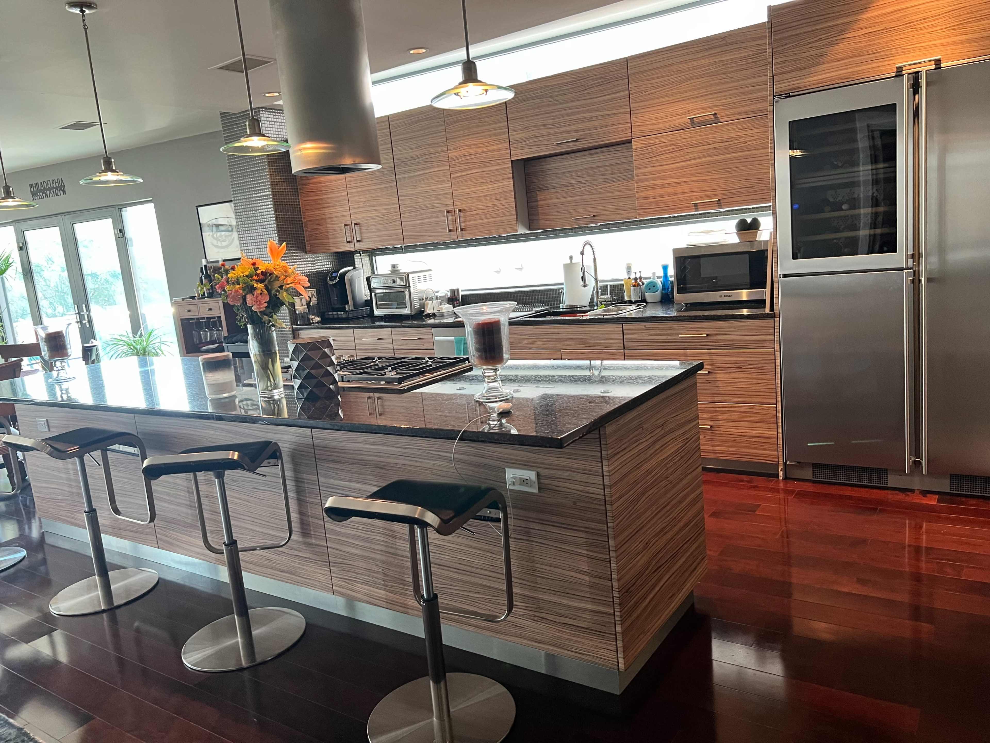 A modern kitchen with a central island, bar stools, stainless steel appliances, and wooden cabinetry.