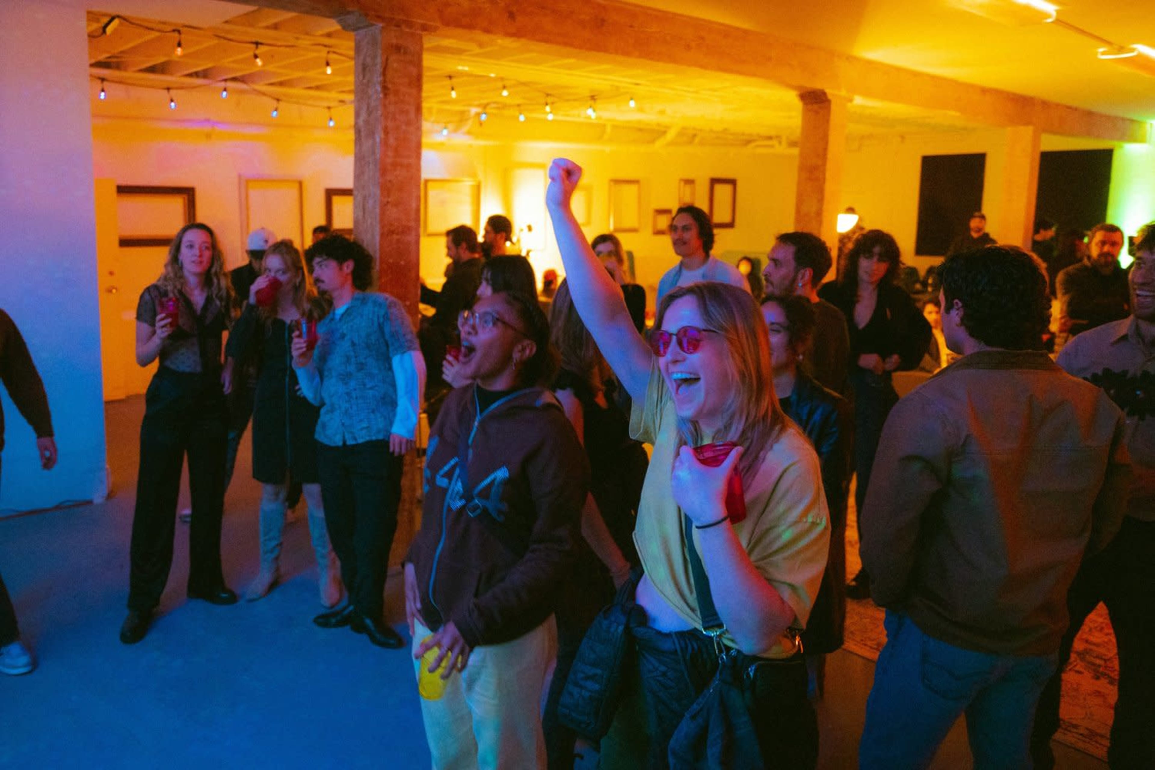 A crowd of people is enjoying a lively indoor party with colorful lighting, engaged in music and conversation.