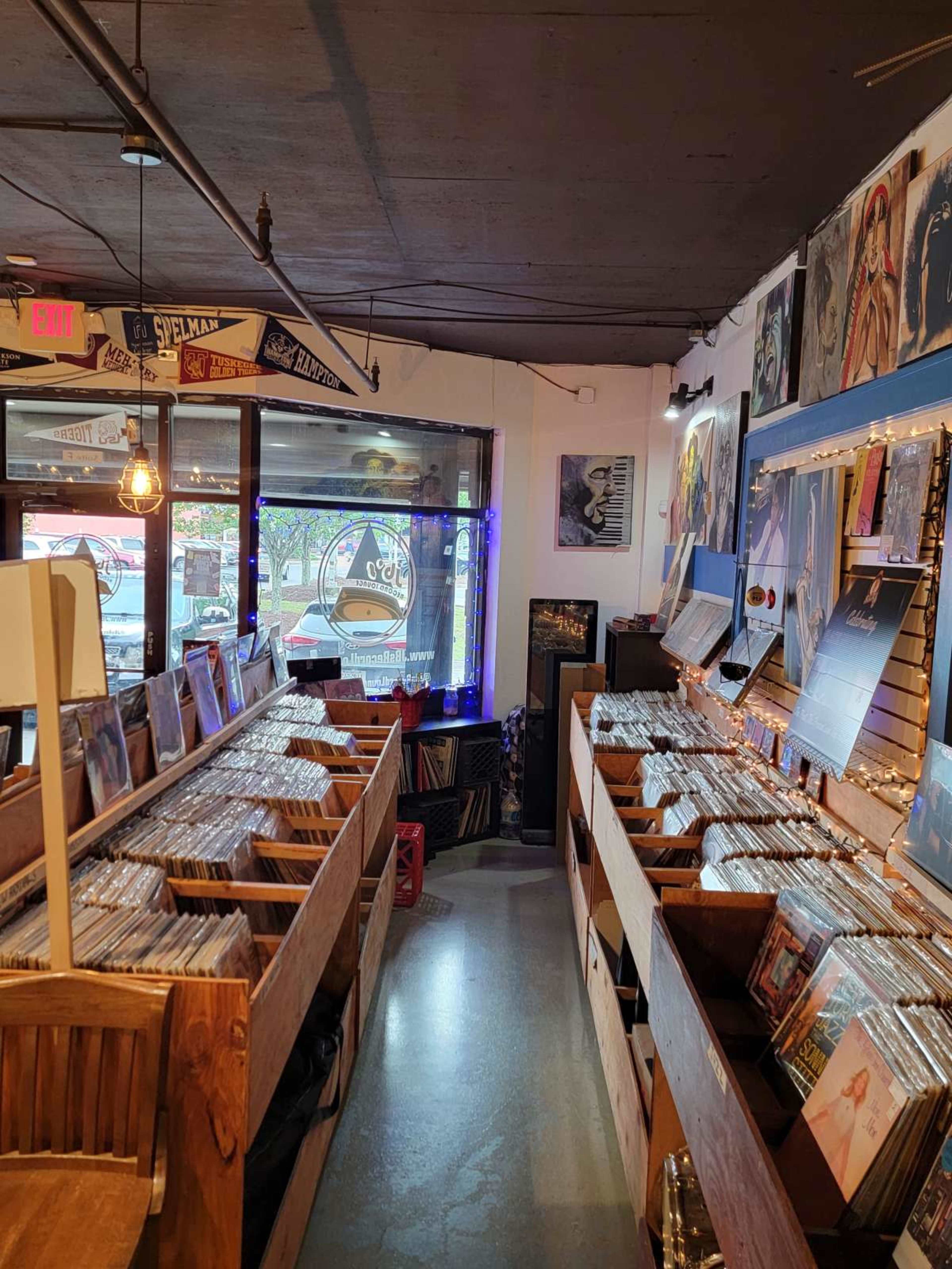 The image depicts a record store with rows of wooden crates filled with vinyl records and artwork displayed on the walls.