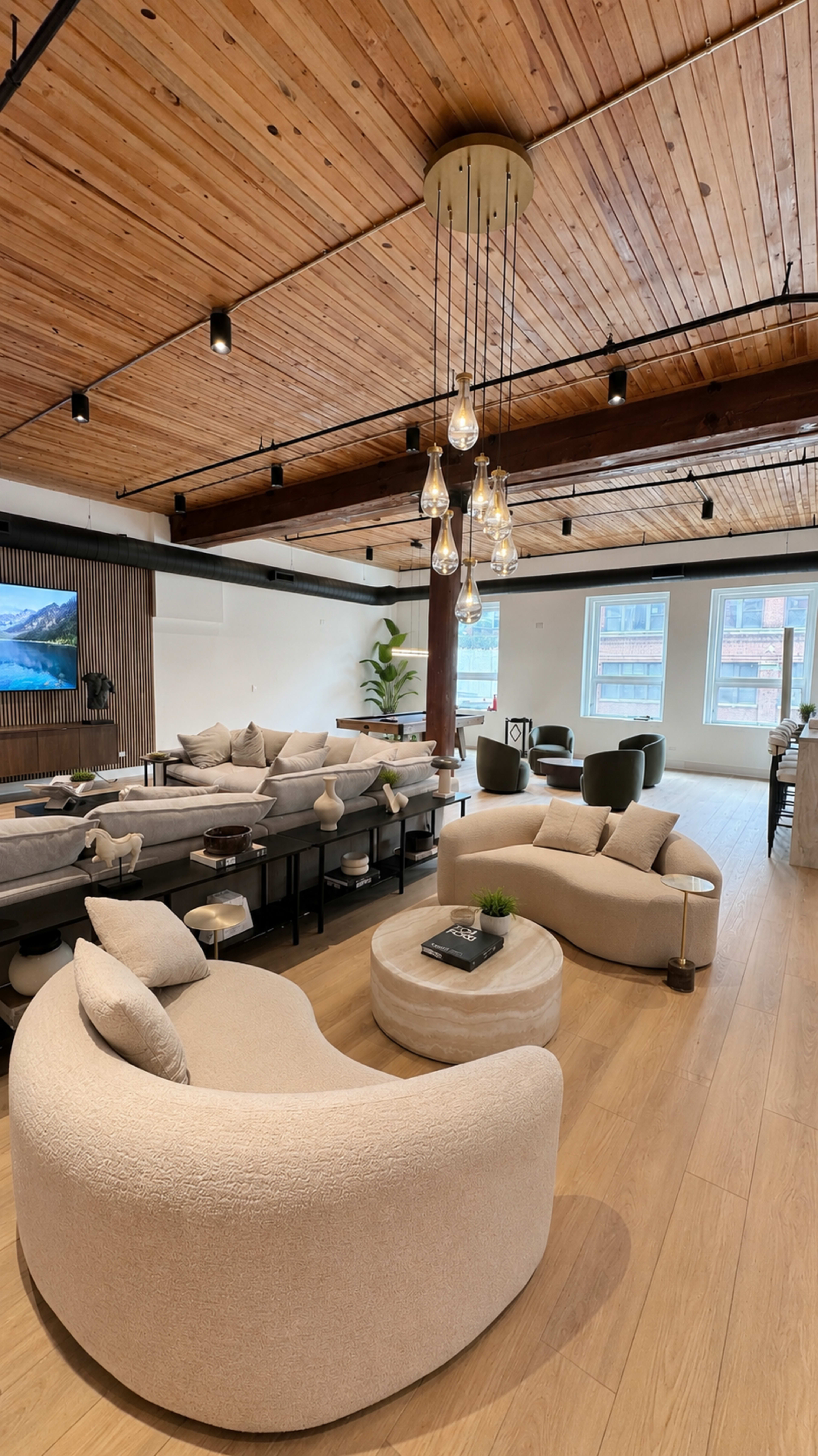 The image features a spacious interior with modern furniture, including two curved sofas, a round coffee table, and large windows allowing natural light to fill the room.