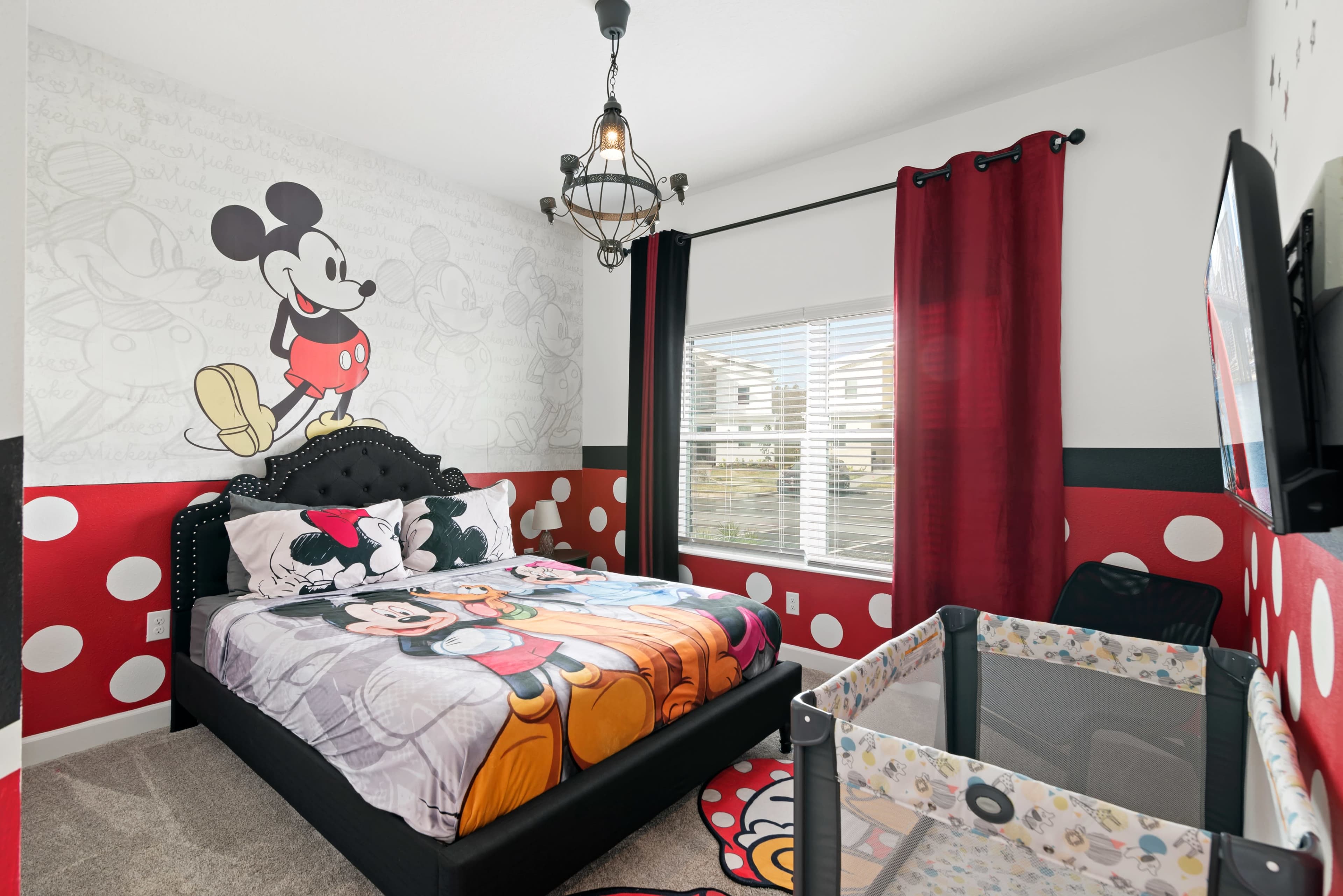 A children's bedroom features a black bed with a Mickey Mouse-themed comforter, red and white polka-dot decor, and a playpen in the corner.