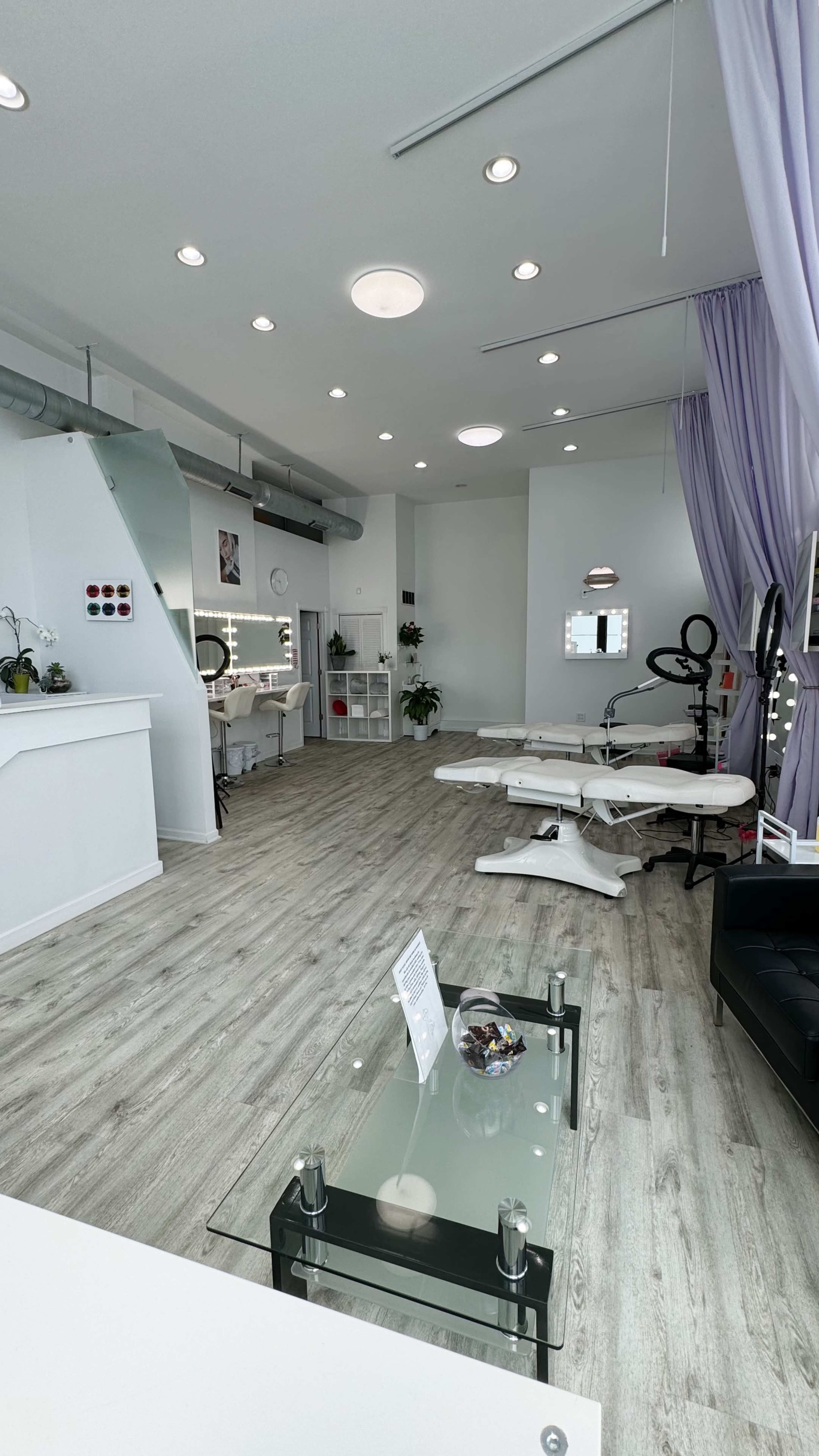A modern salon interior with wooden floors, a reception area, treatment chairs, and purple curtains.