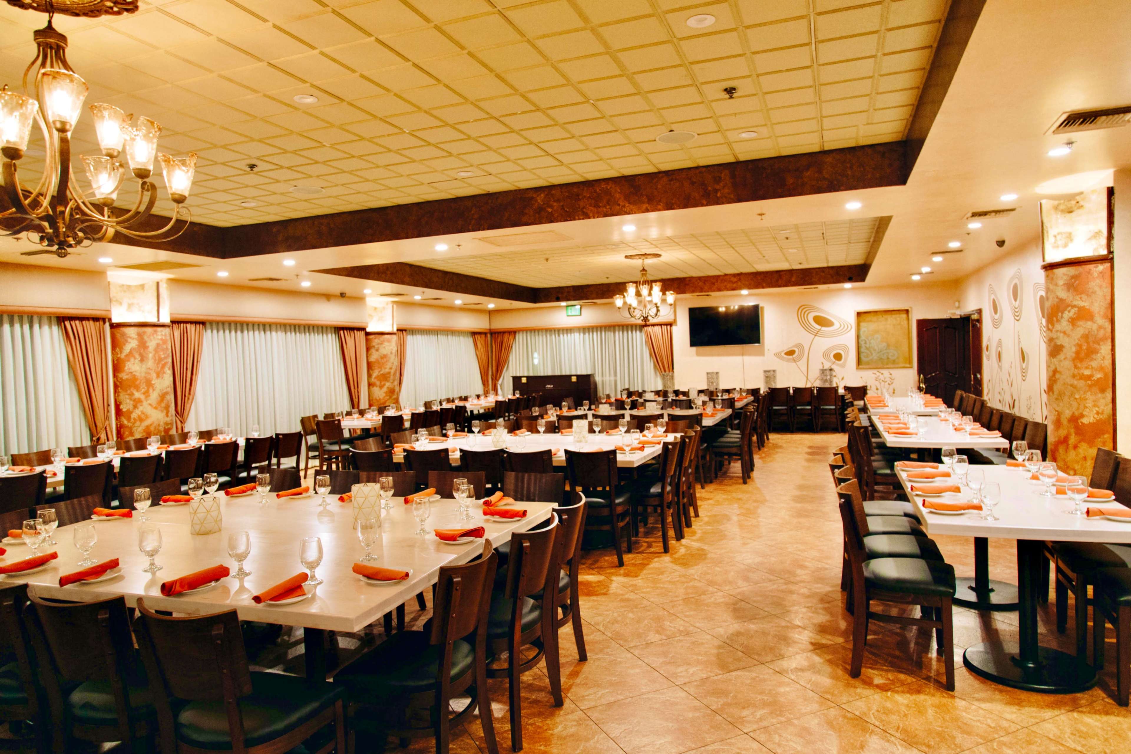 A spacious restaurant interior with round tables set for dining and a softly lit chandelier overhead.