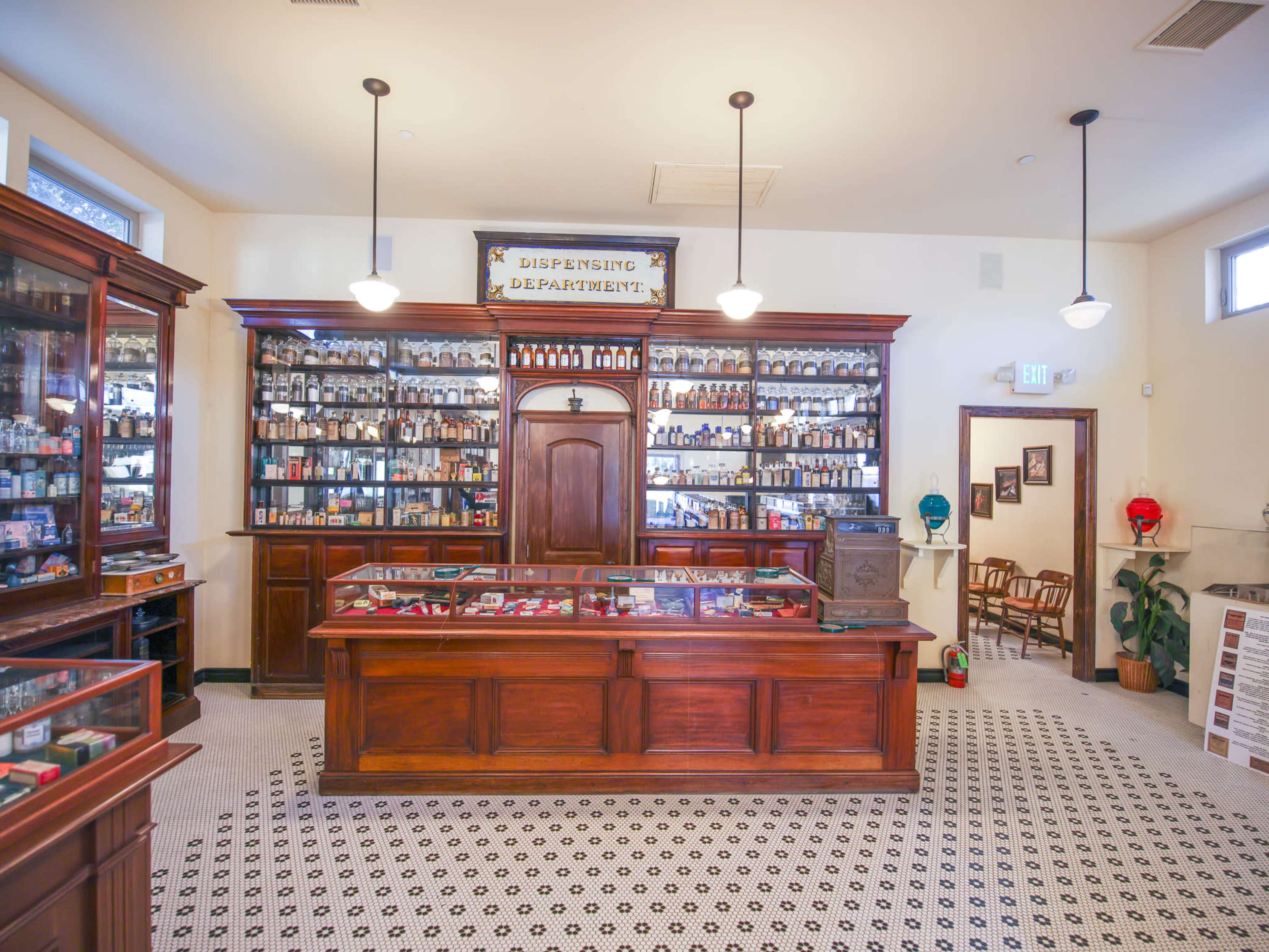 An antique pharmacy interior featuring wooden cabinets filled with bottles and a central dispensing counter.