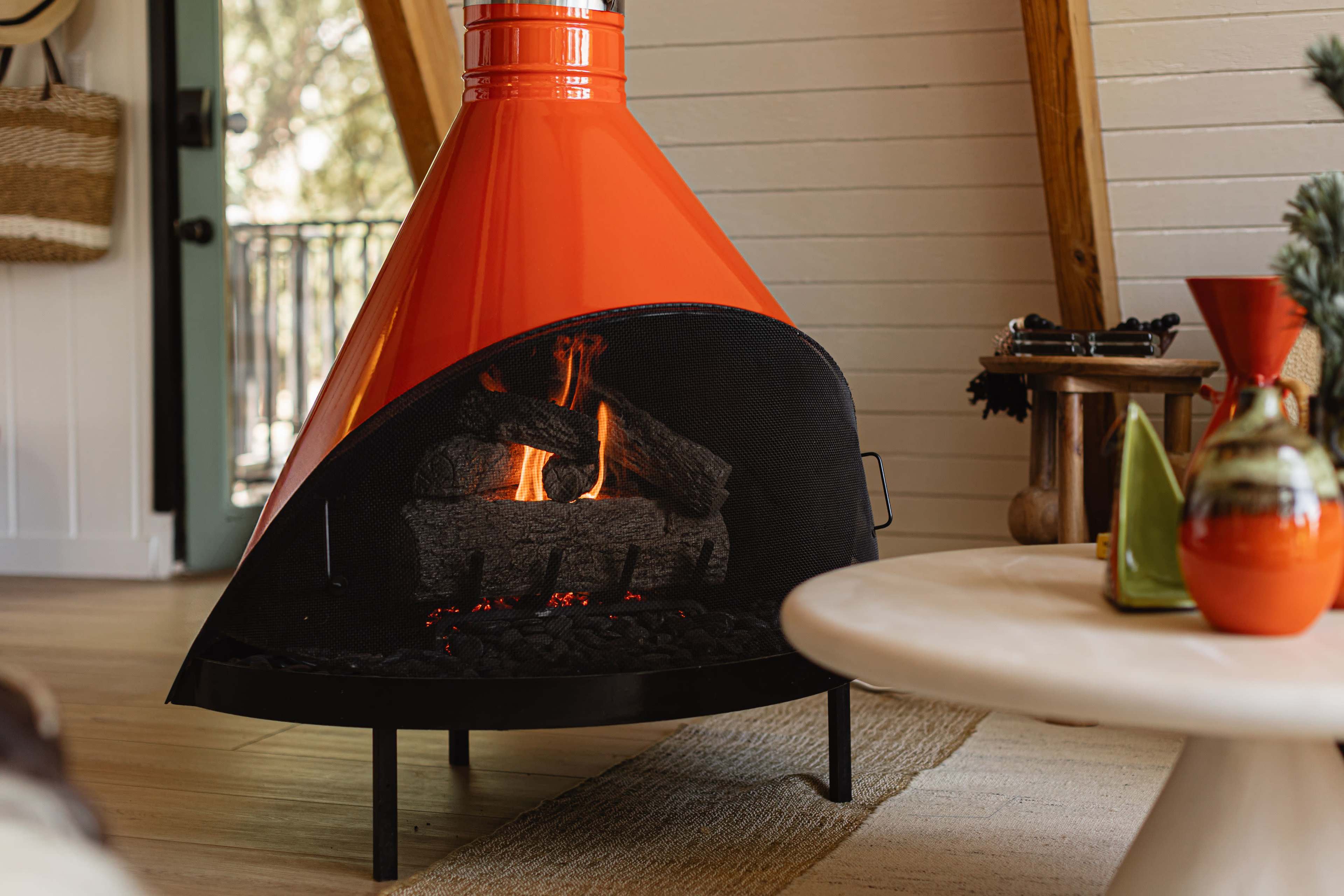 A modern, orange freestanding fireplace with visible flames is positioned in a cozy living room setting.
