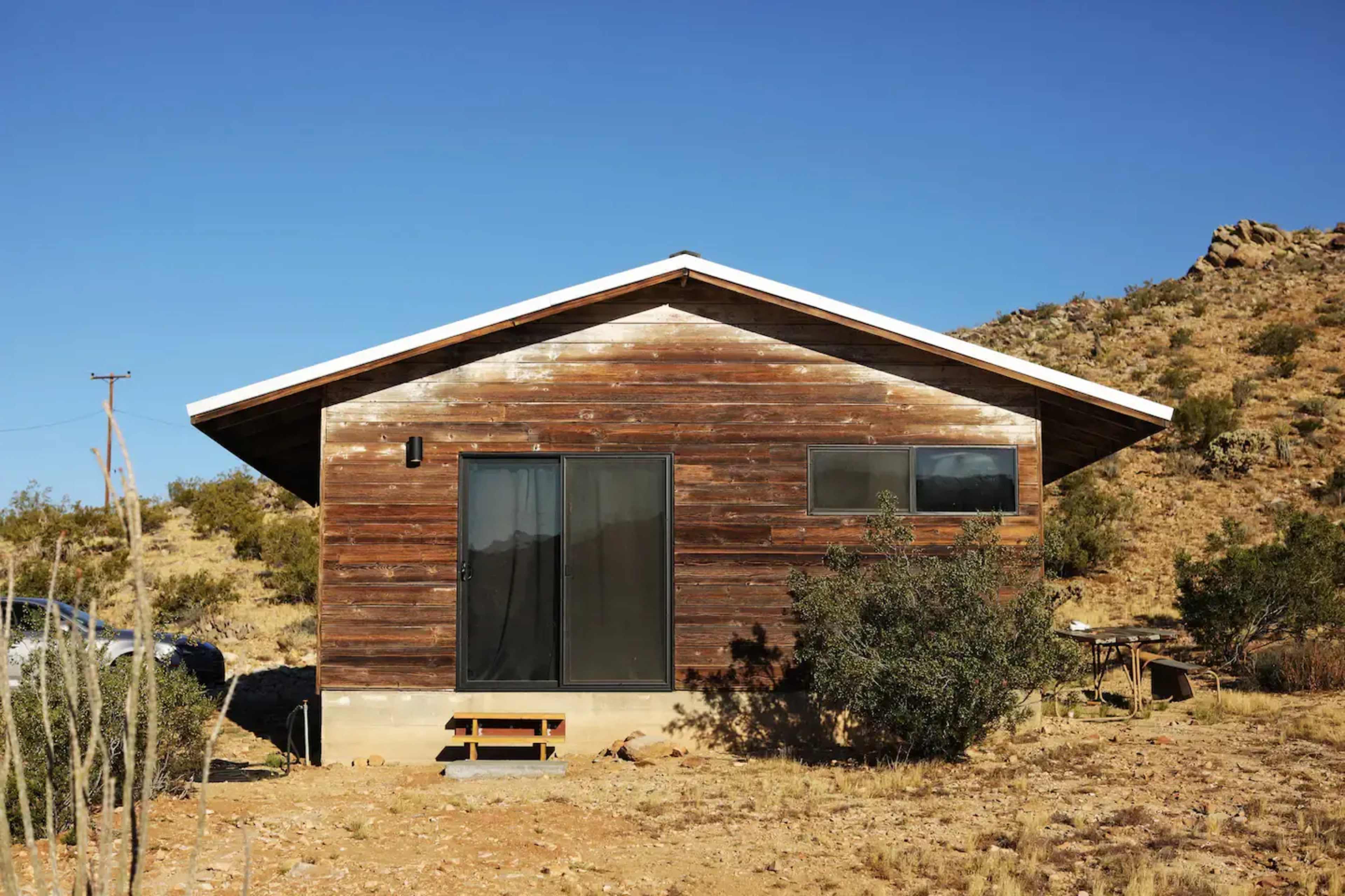 A modern wooden house with a sloped roof stands on a rocky landscape under a clear blue sky.