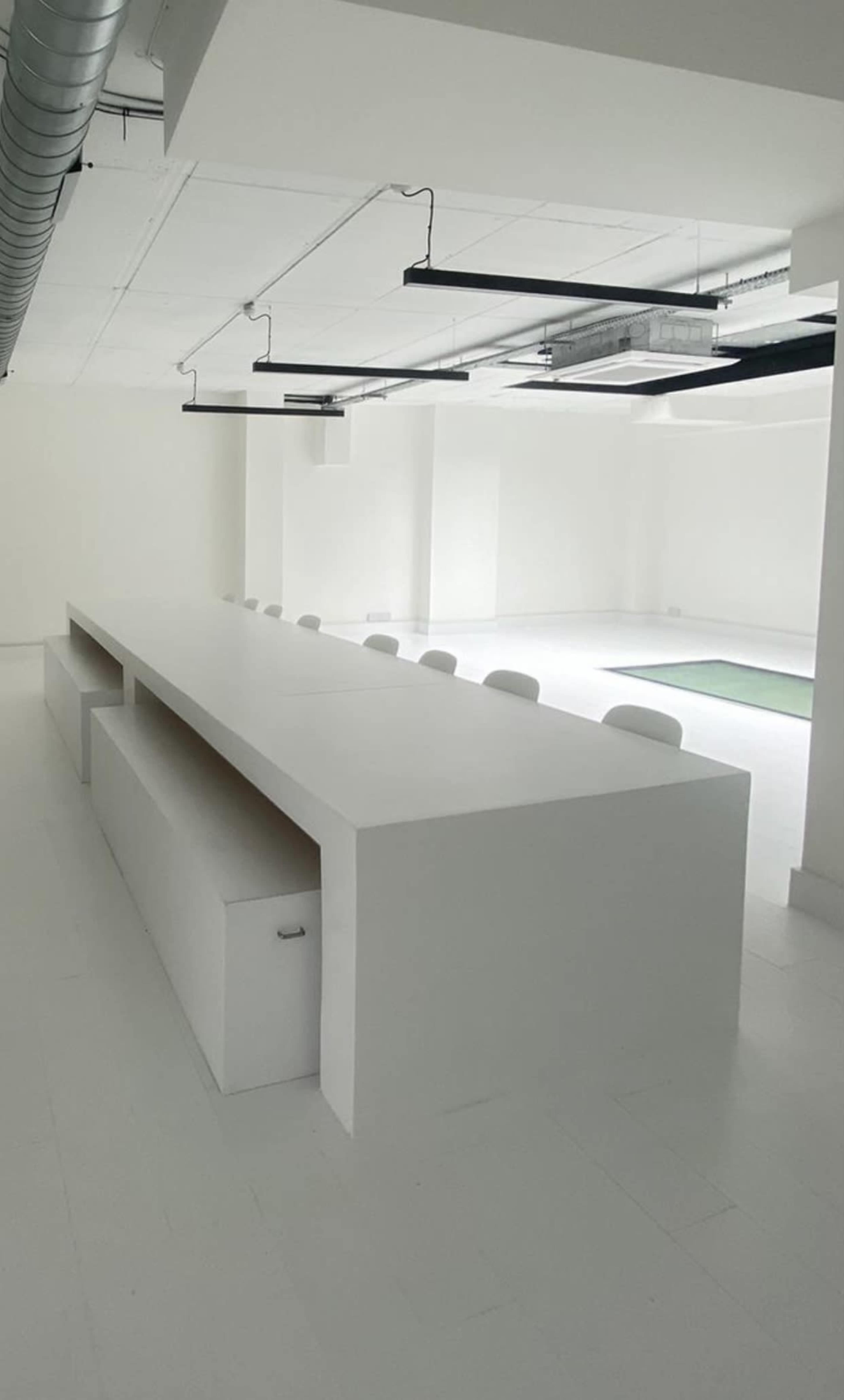 A spacious, minimalistic office interior with a long white table and several chairs arranged around it.