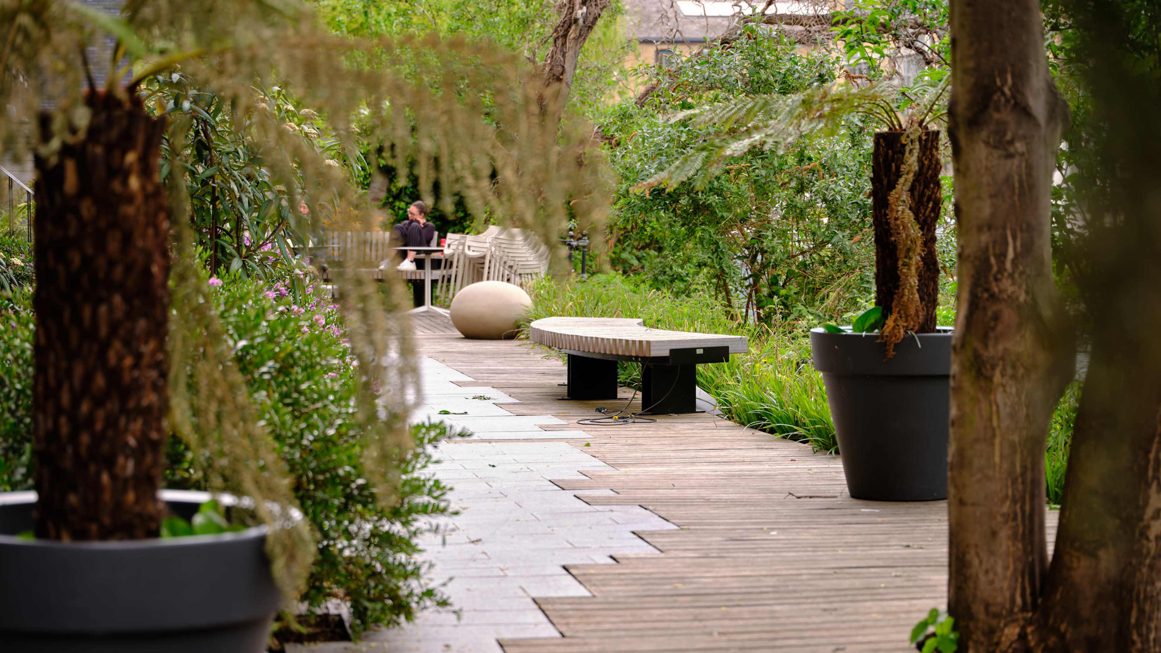 A garden path lined with planters and benches, surrounded by greenery and trees.