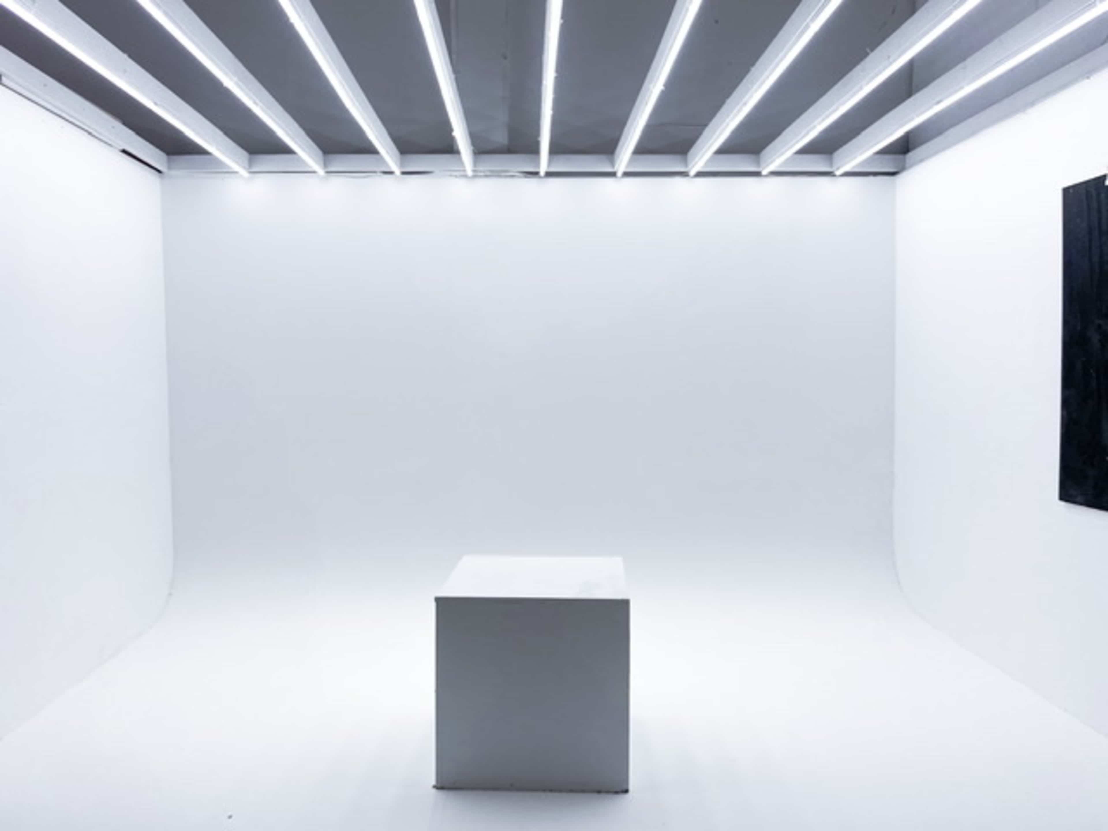 A white room with a simple square pedestal under bright, linear ceiling lights.