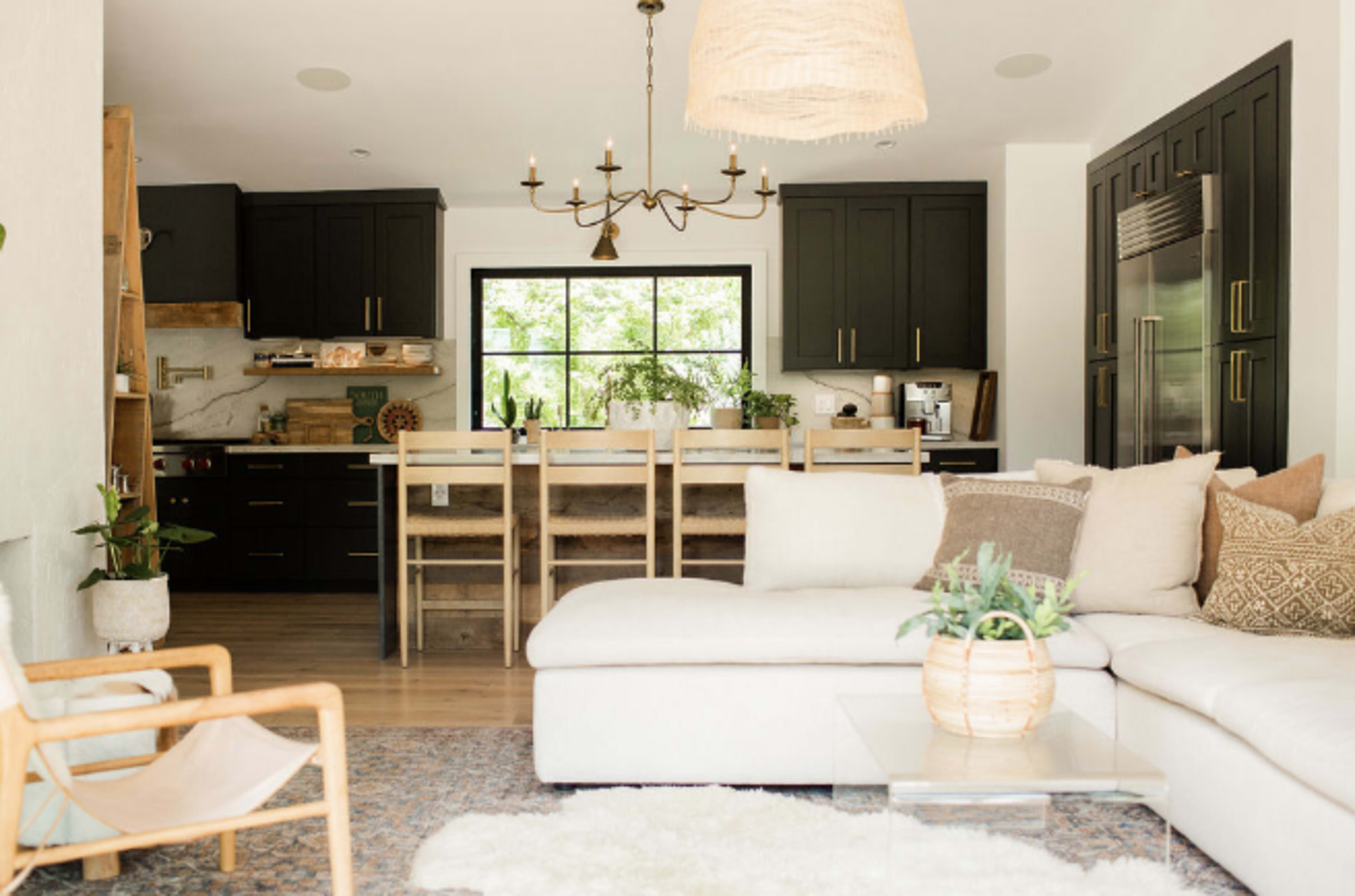 The image shows a modern kitchen and living area with black cabinetry, a large window, and a sectional sofa arranged around a glass coffee table.