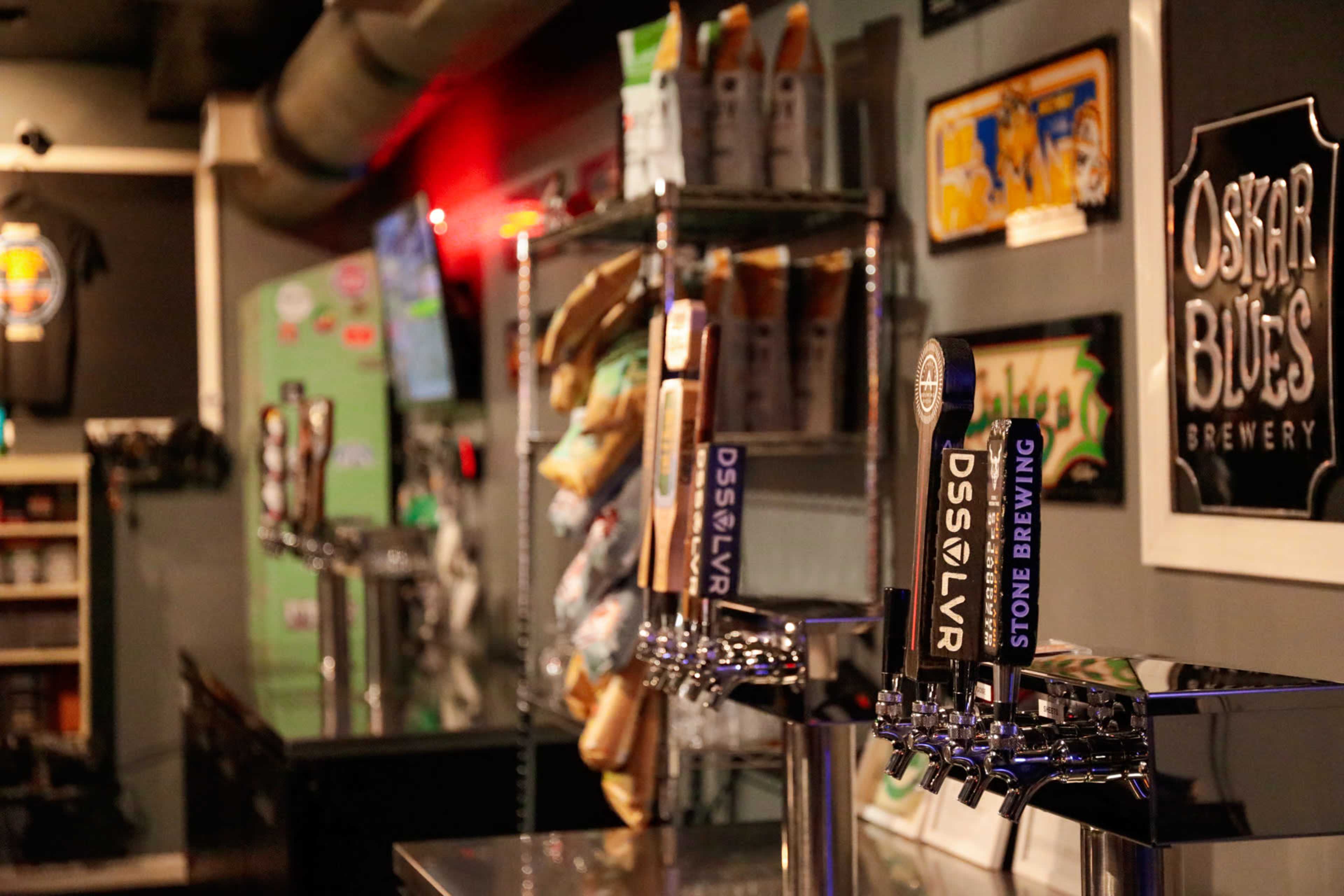 A row of beer taps stands prominently against a bar, with branded merchandise and packaged goods displayed on shelves in the background.