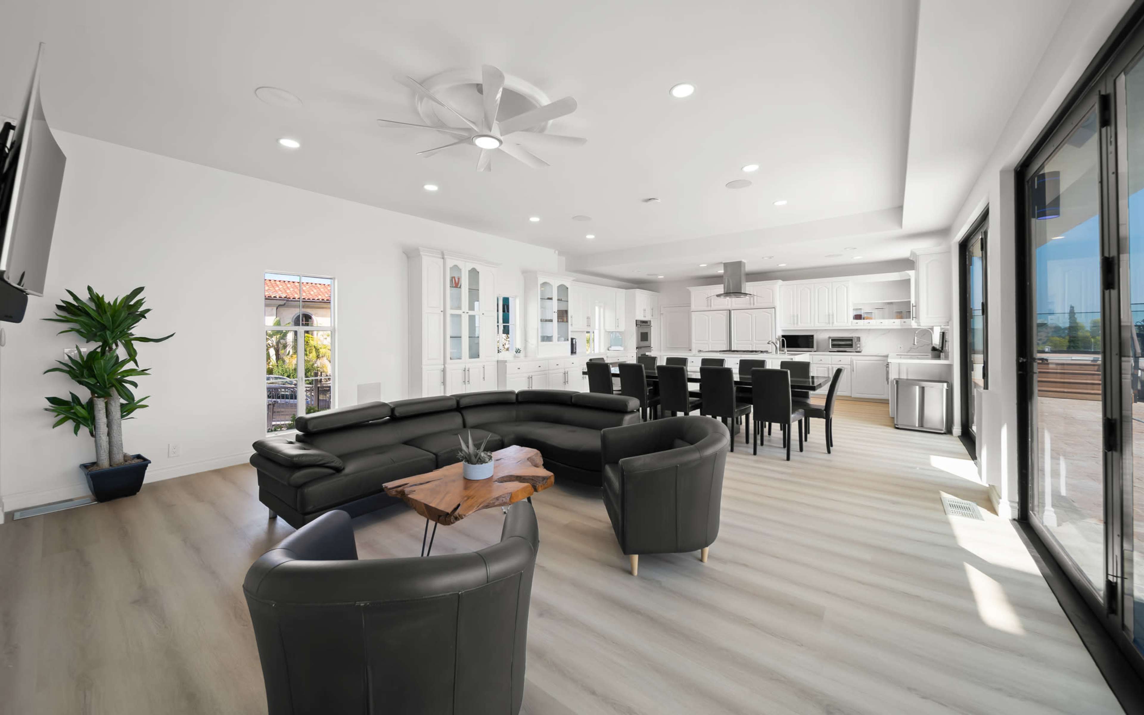 A modern open-concept living space features a black sectional sofa, a wooden coffee table, and a dining area with black chairs adjacent to a bright kitchen.
