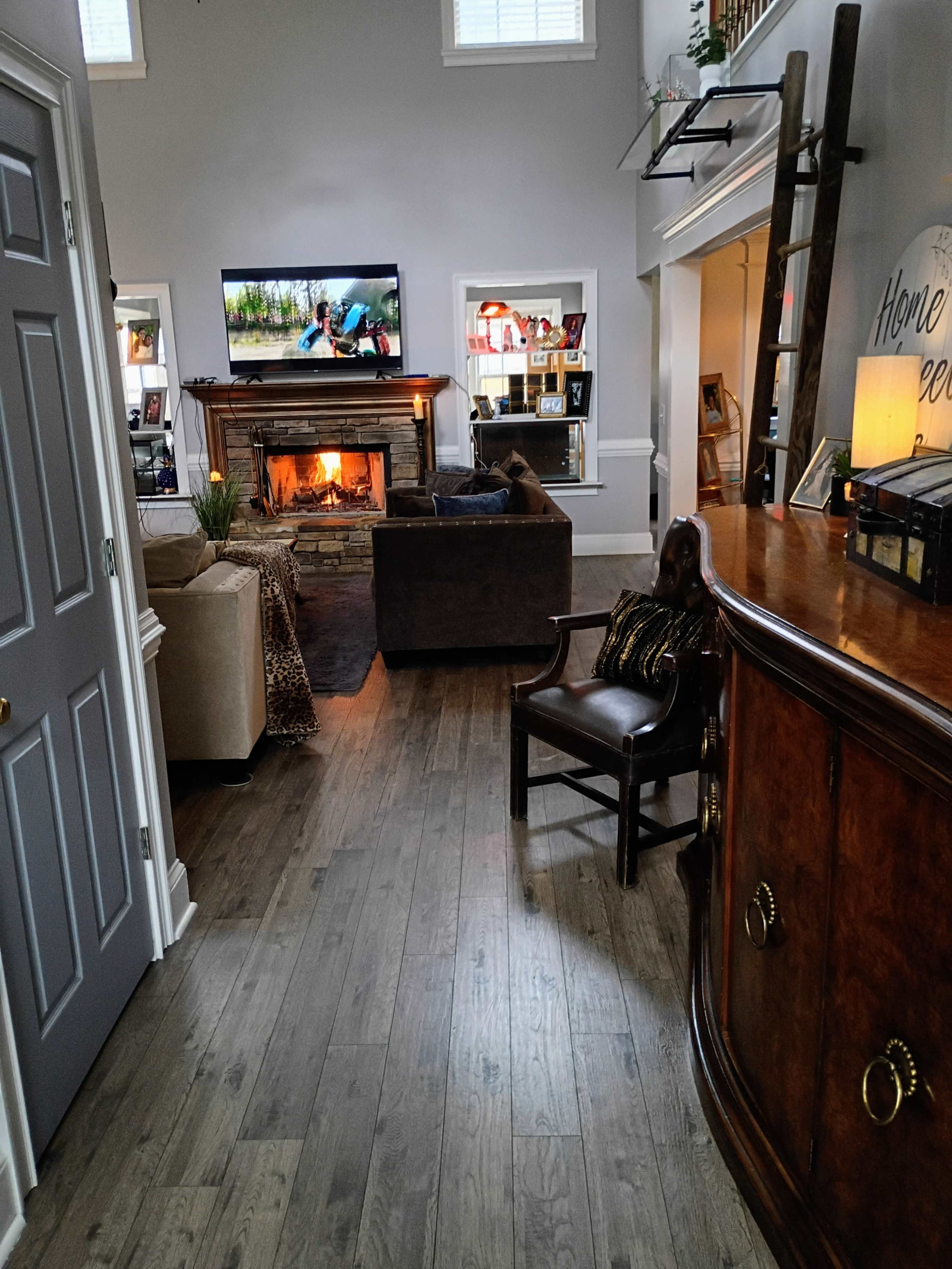 A spacious living room features a fireplace, a television mounted above it, and various seating options, including a sofa and an armchair.