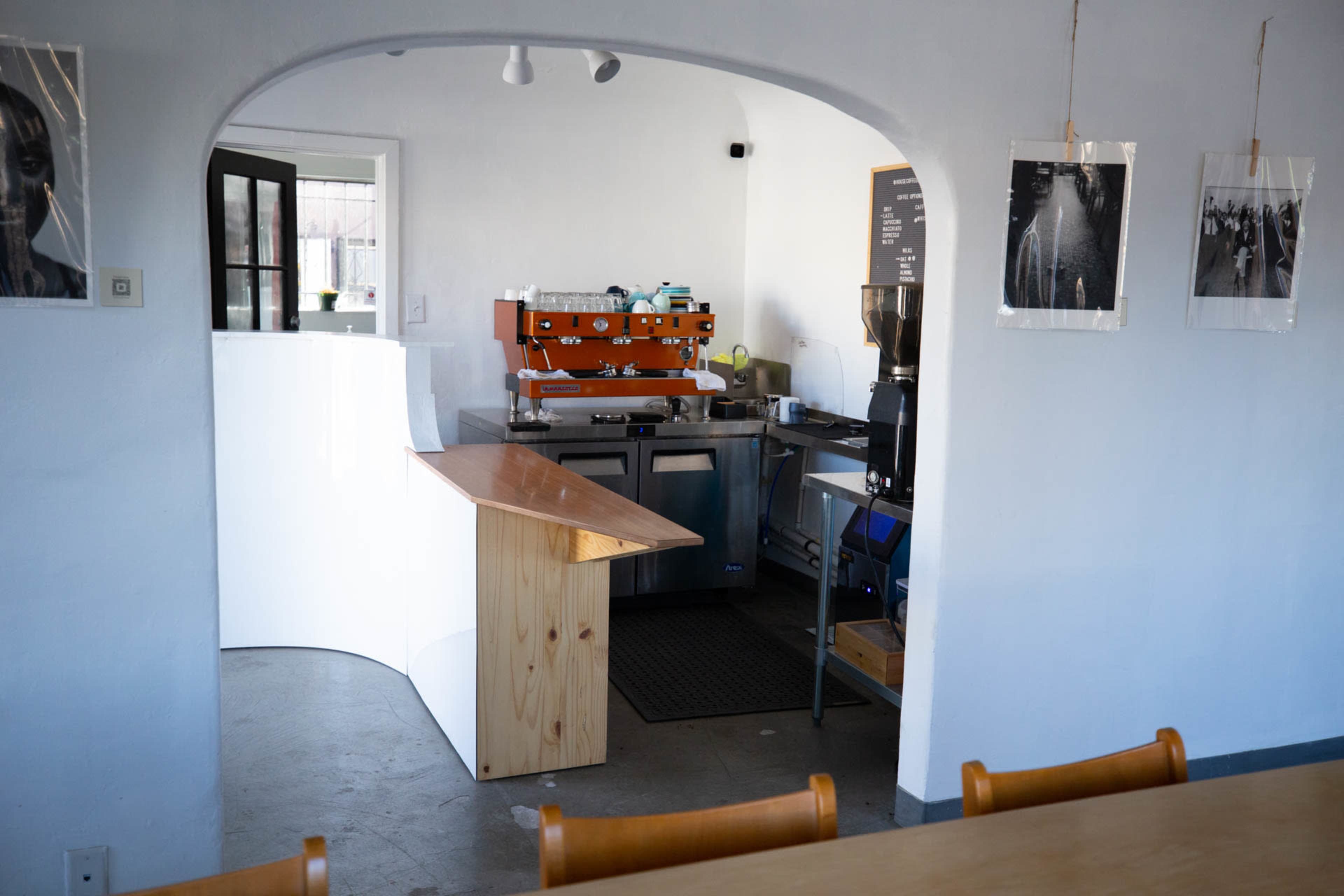 A modern coffee shop interior with a wooden counter, espresso machine, and photographs on the walls.