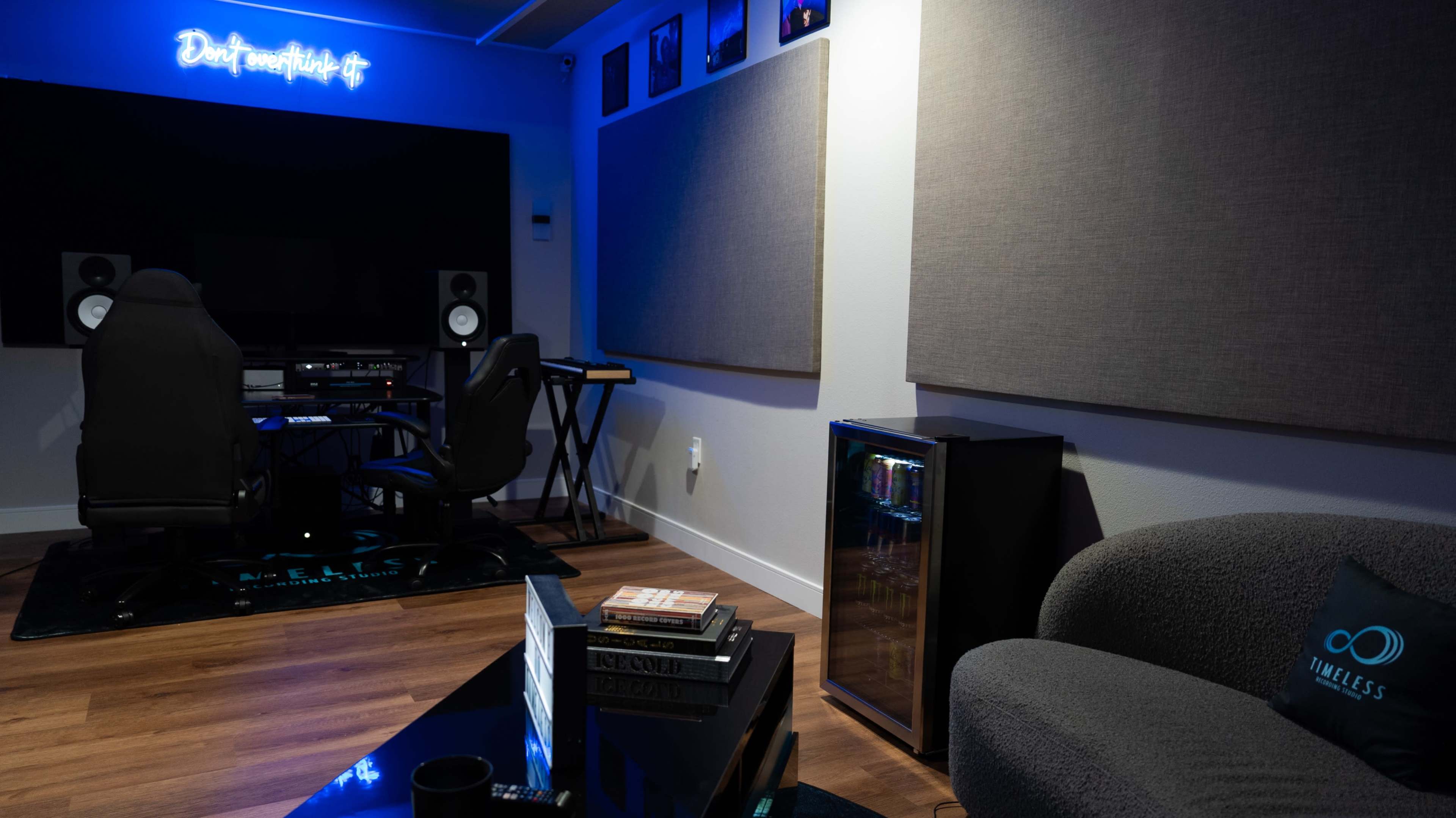 The image shows a modern home studio with a desk, speakers, and a seating area, illuminated by blue lighting.