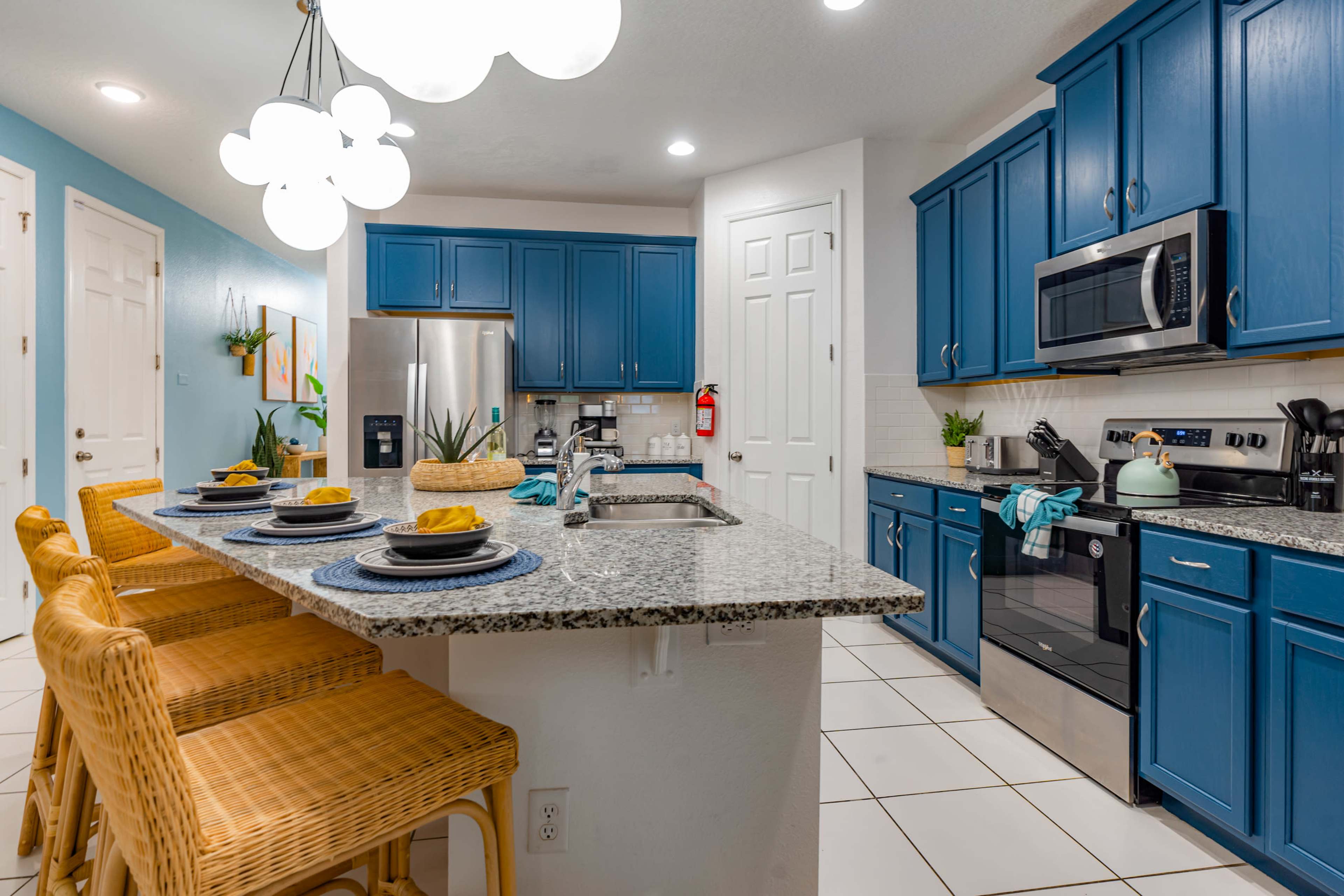 The image shows a modern kitchen featuring blue cabinets, a granite countertop with bar stools, and stainless steel appliances.