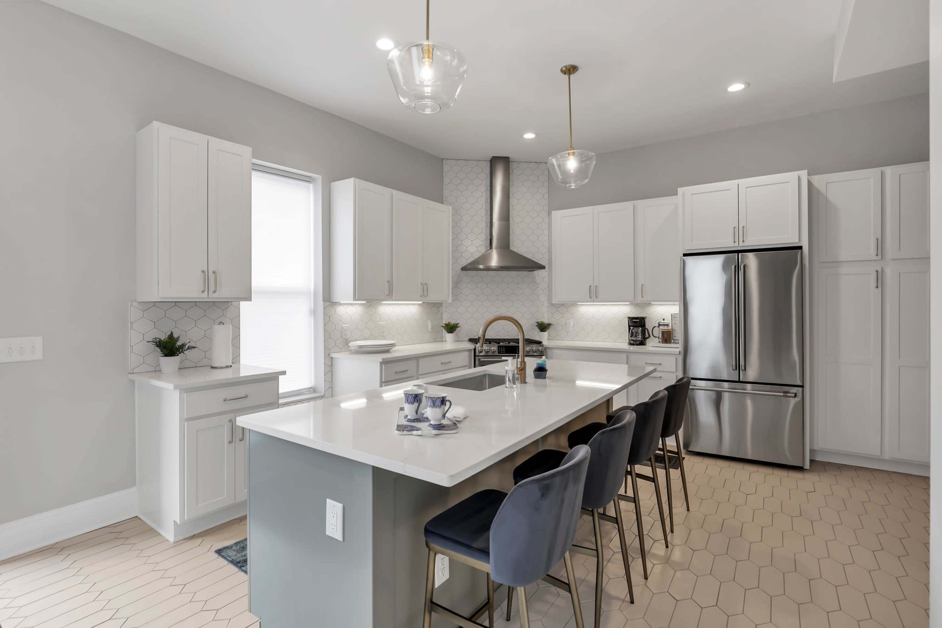 A modern kitchen features light gray walls, white cabinetry, a large island with seating, and stainless steel appliances.