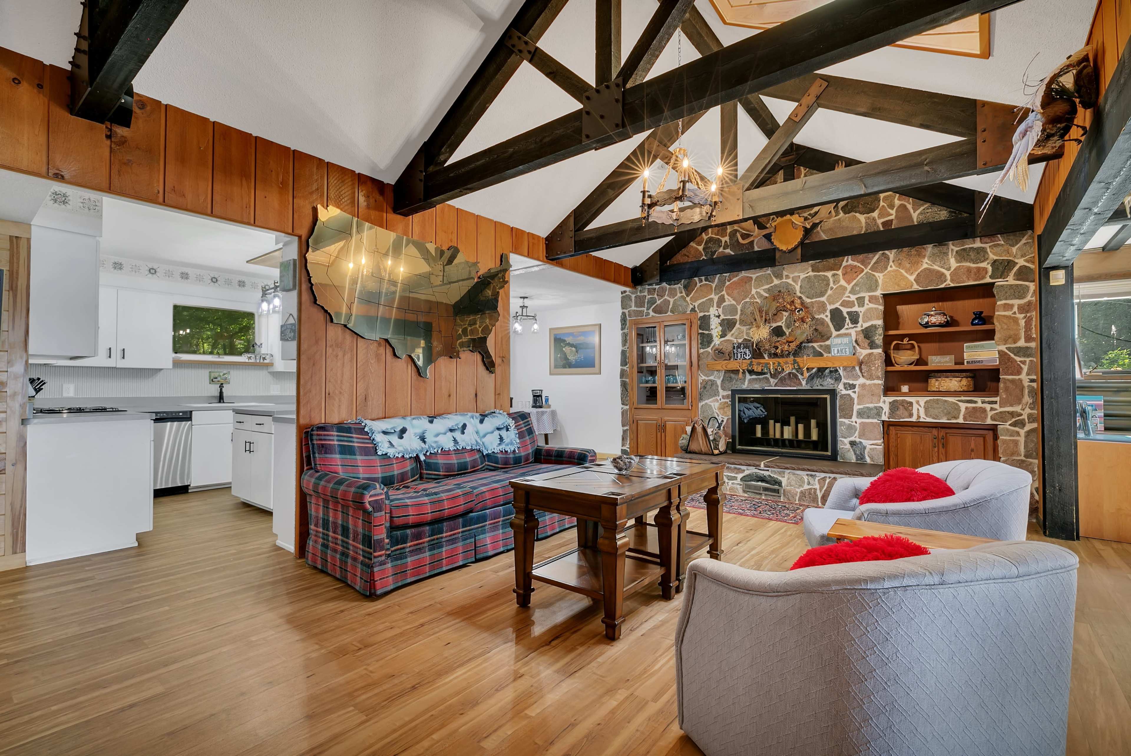The living room features a stone fireplace, wooden beams, and a plaid sofa with a wooden coffee table.
