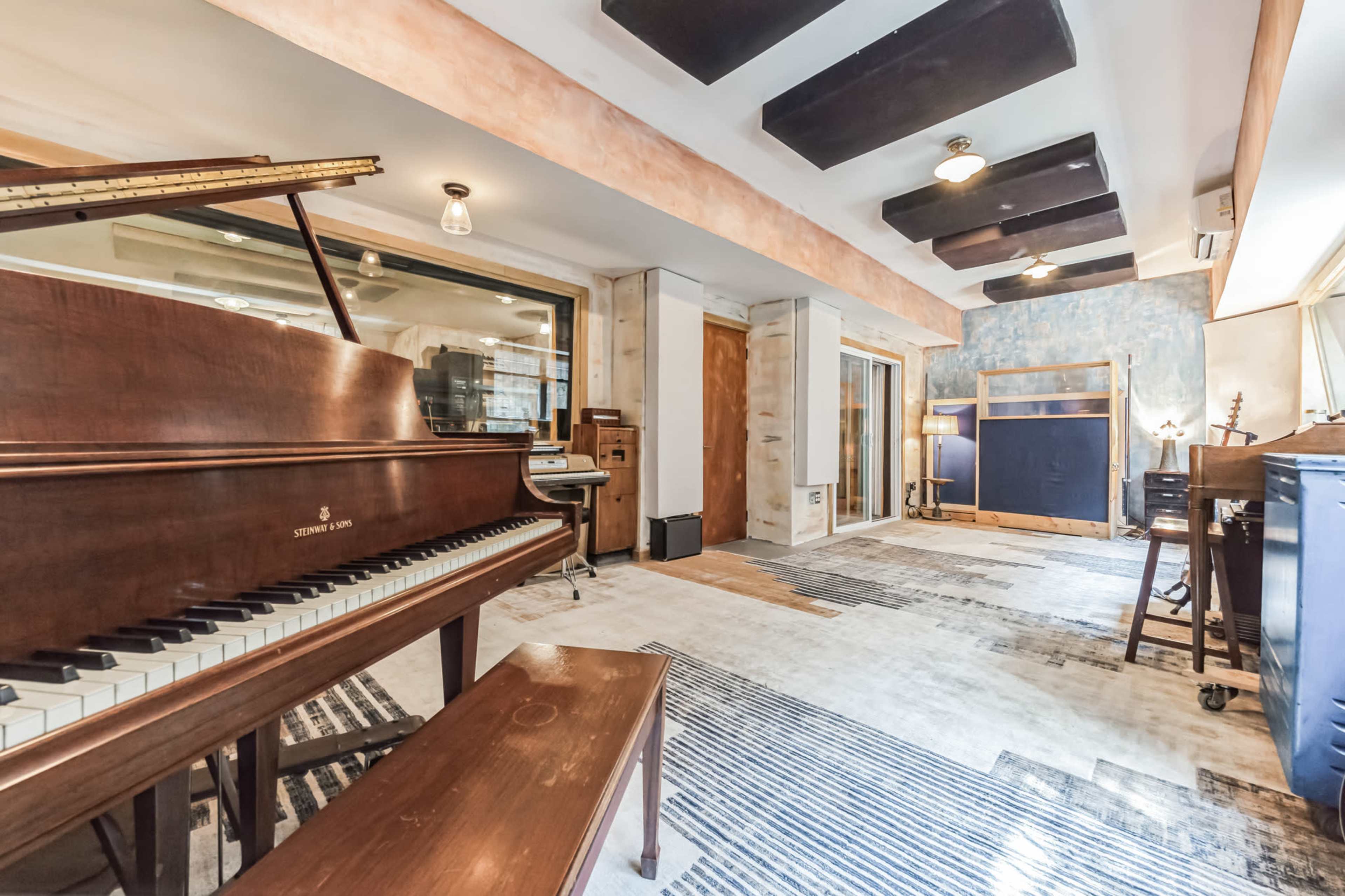 A music studio featuring a grand piano, acoustic panels on the ceiling, and various instruments arranged in a spacious layout.