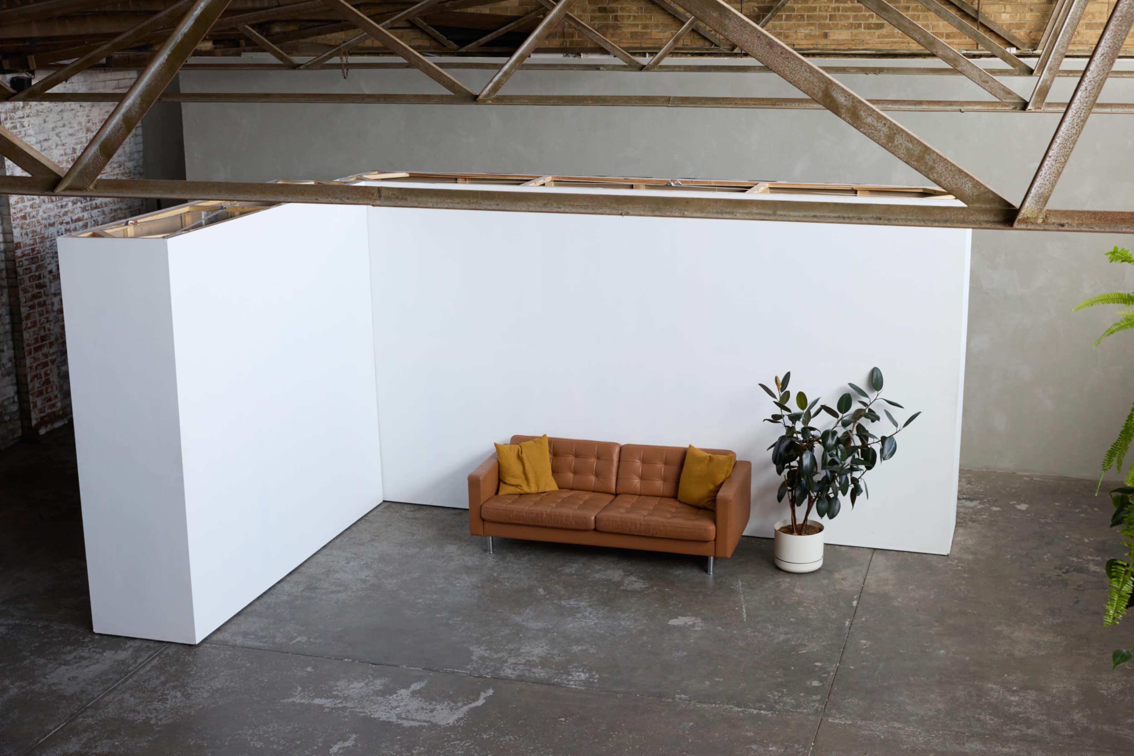 A modern, minimalist space with a brown sofa and a potted plant against a white wall in an industrial setting.