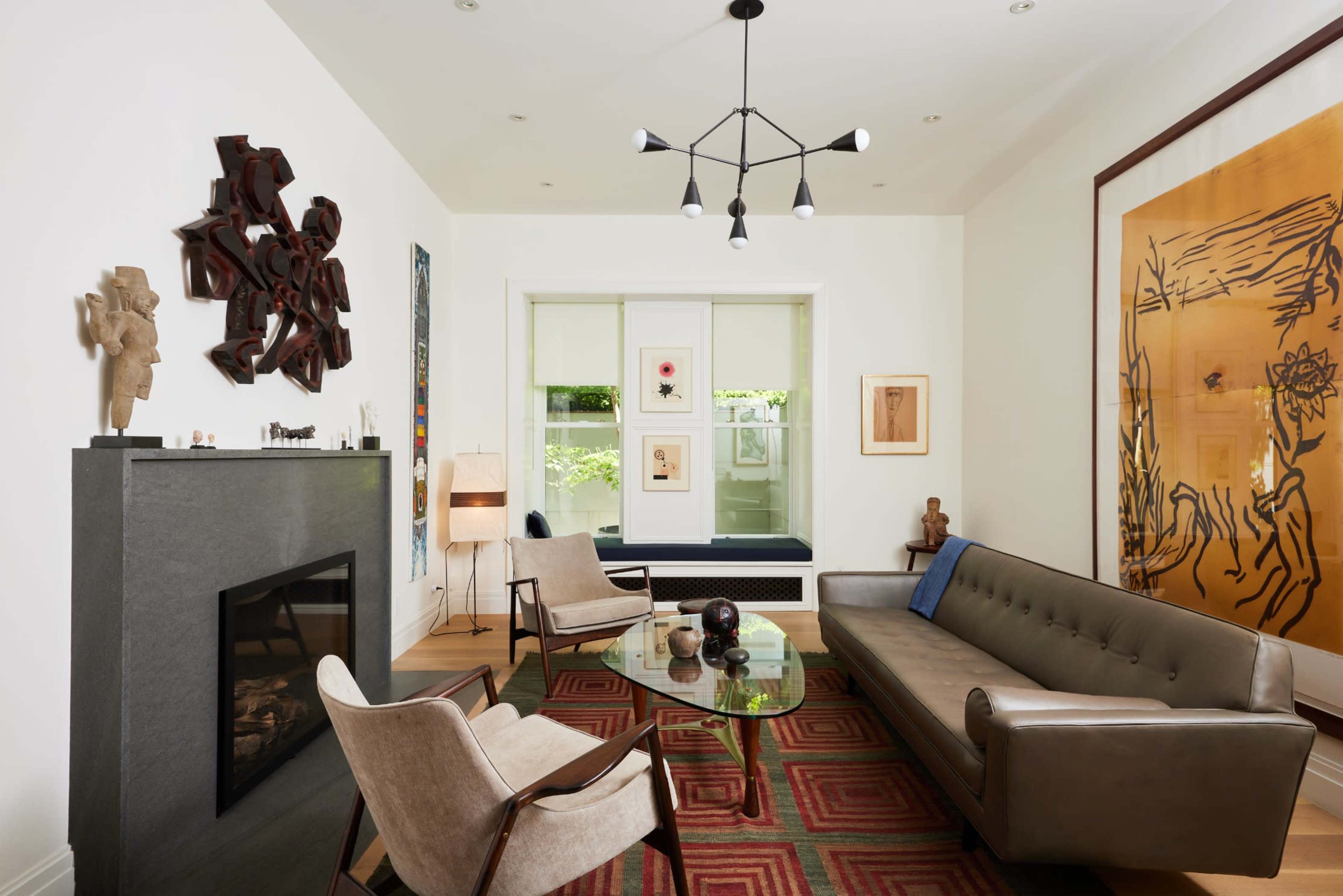 The image shows a modern living room with a beige sofa, a glass coffee table, and an art-adorned wall featuring various sculptures and framed artwork.