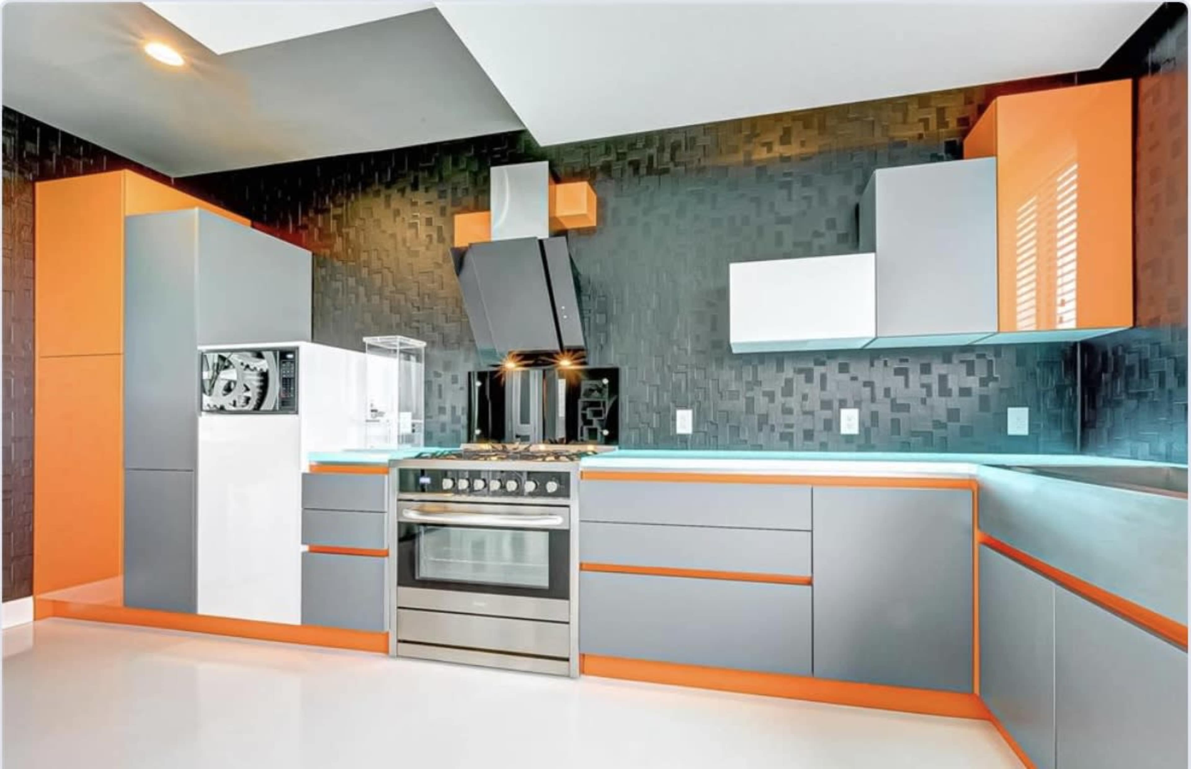 A modern kitchen features gray cabinets with orange accents, a built-in refrigerator, and a stainless steel stove with a hood.