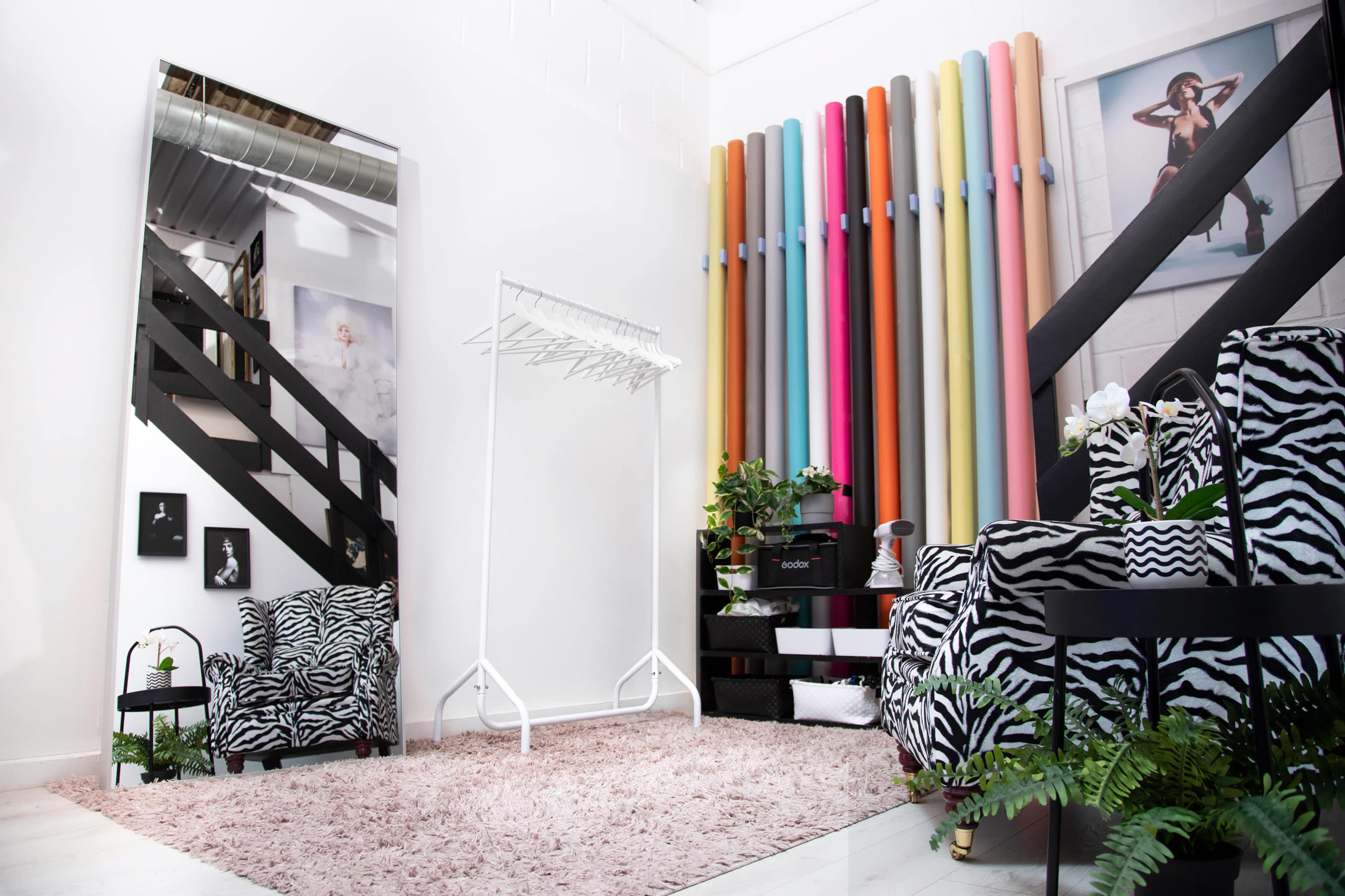 The image shows a stylish interior space featuring a white wall with colorful vertical poles, a mirrored wall, and zebra-striped furniture arranged around a plush rug.