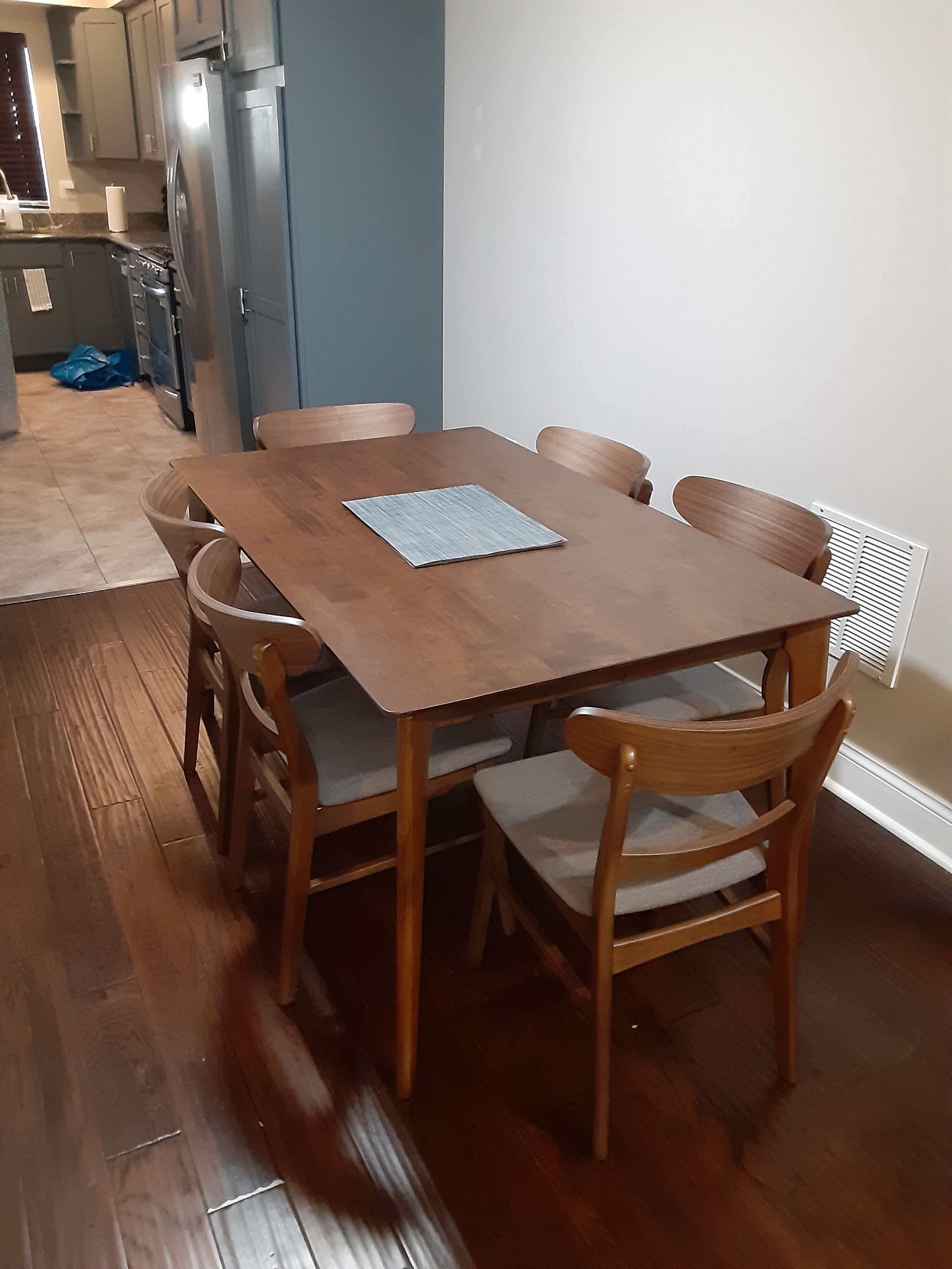 A wooden dining table with six chairs is set in a kitchen area, next to cabinets and appliances.