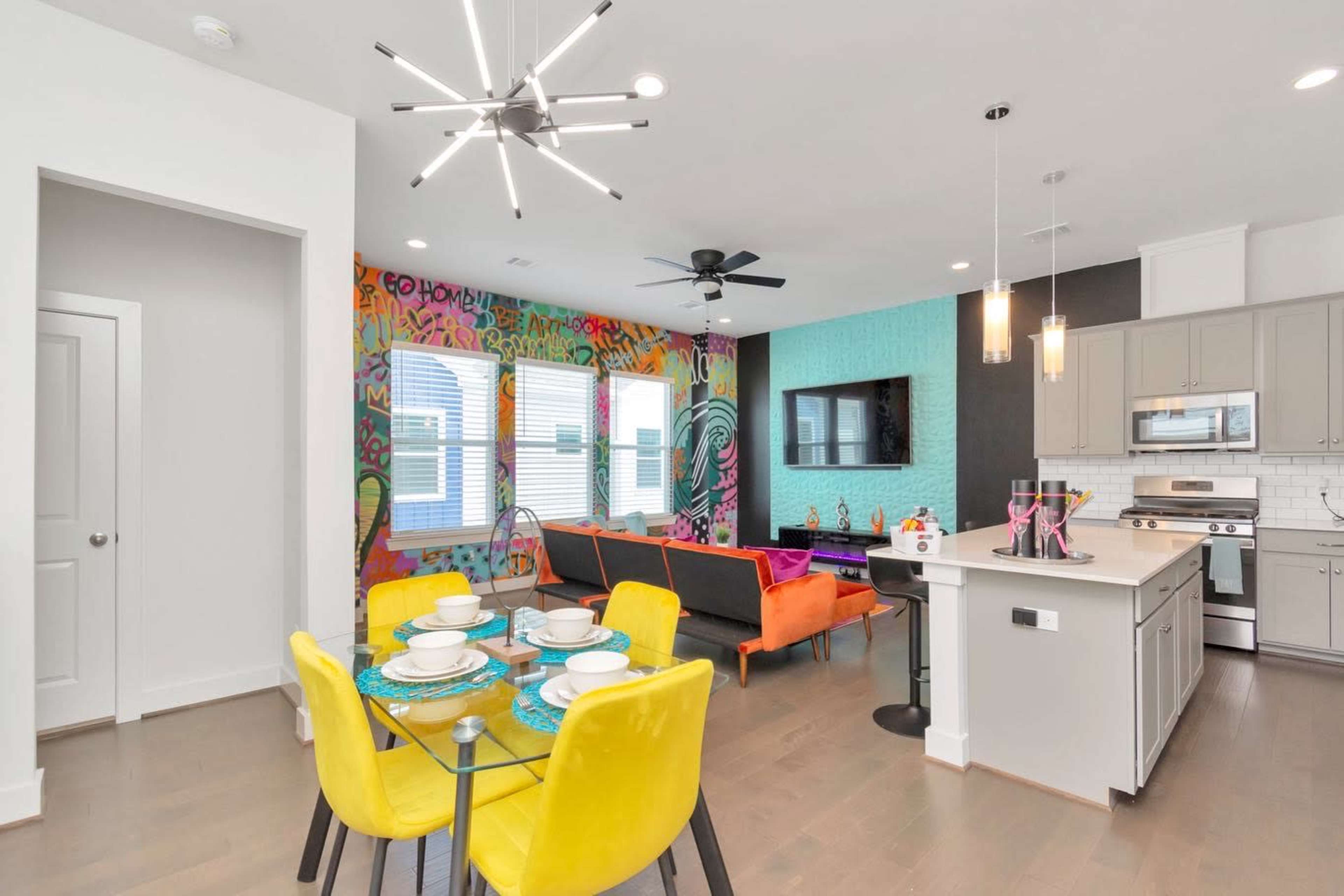A modern open-concept living and dining area with vibrant wall art, a table set for dining, and colorful furniture arrangements.
