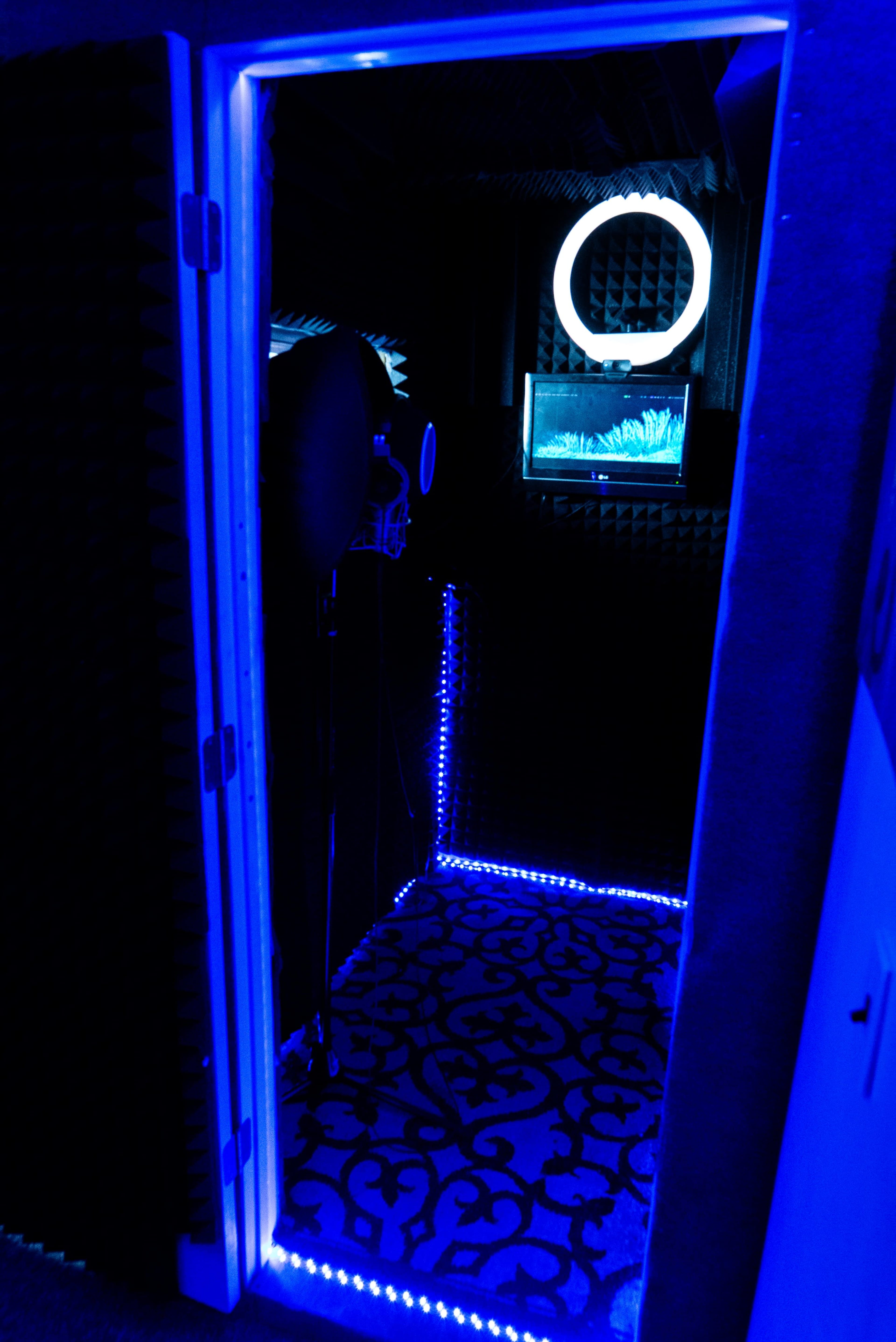The image shows the entrance to a recording booth illuminated with blue lights, featuring soundproofing panels and a microphone setup inside.