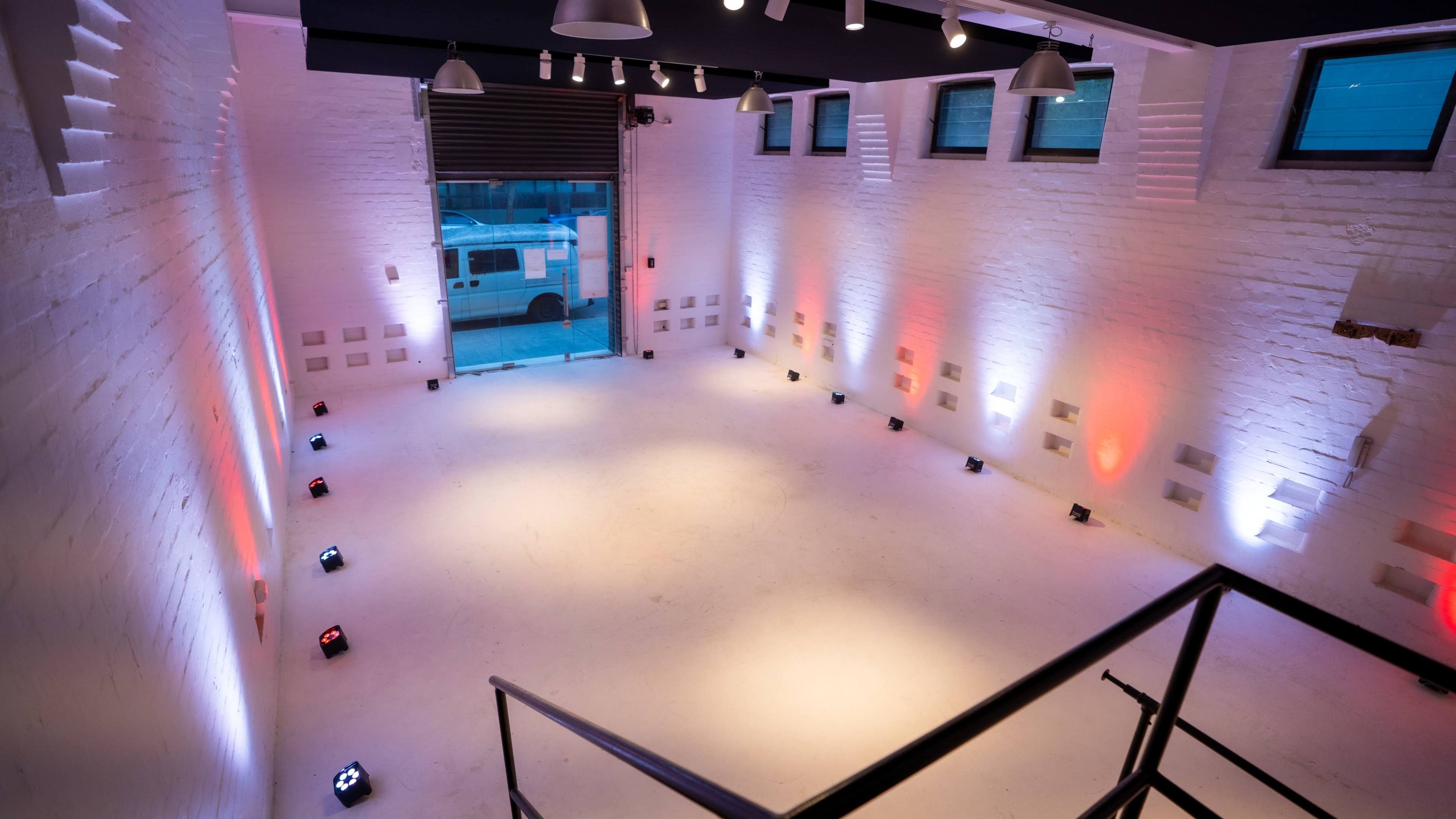 A spacious, well-lit room with white brick walls and a concrete floor, featuring multiple colored lights positioned along the perimeter.