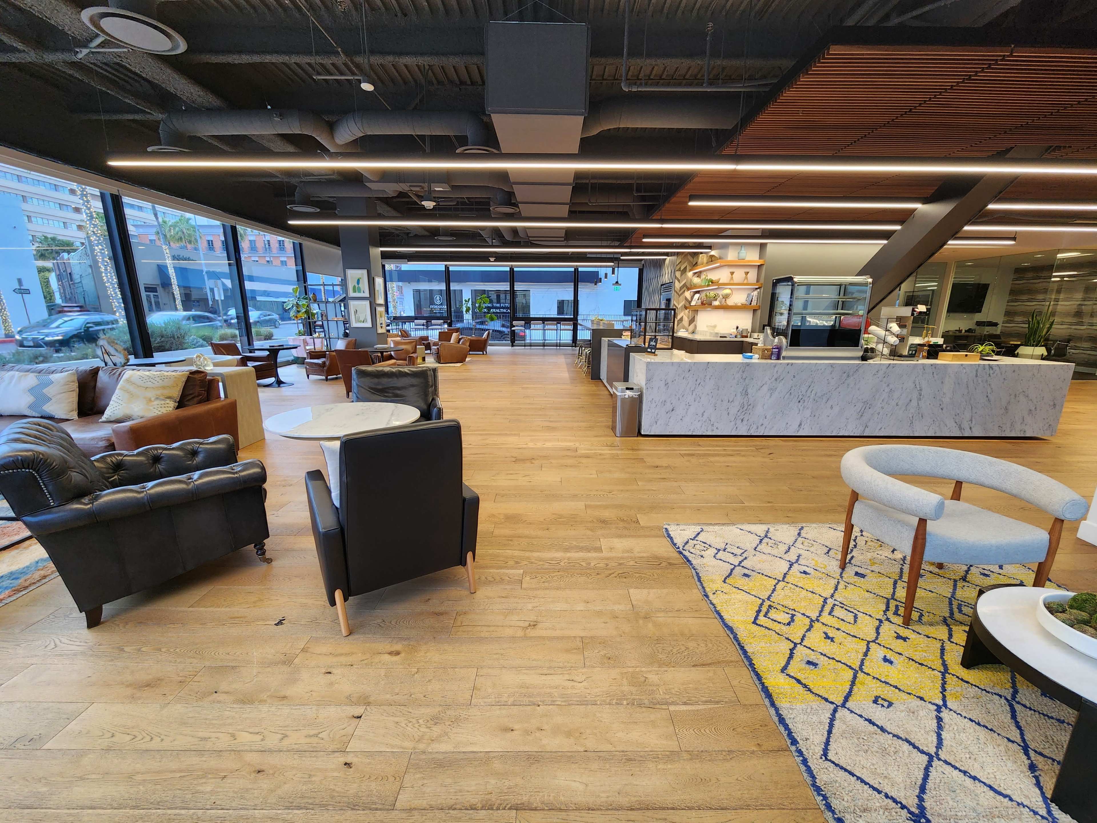A modern café interior with wooden floors, various seating arrangements, and a service counter featuring a marble top and glass display.