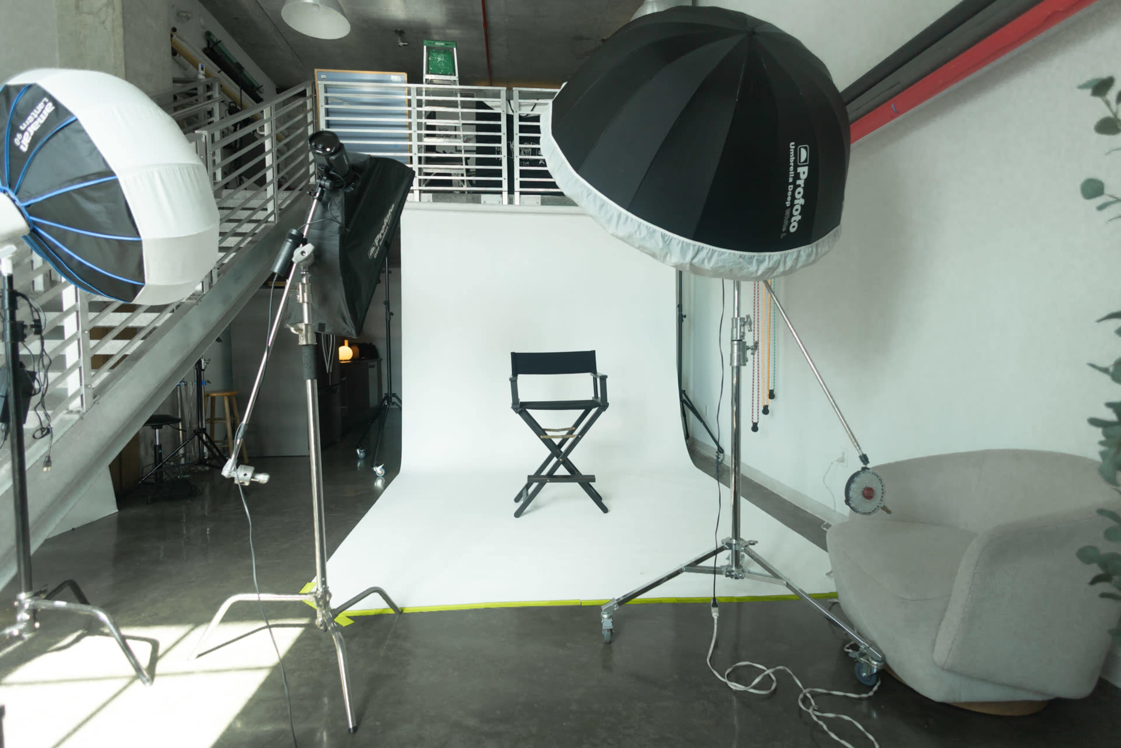 The image shows a photography studio setup featuring lighting equipment, a director's chair, and a neutral backdrop.