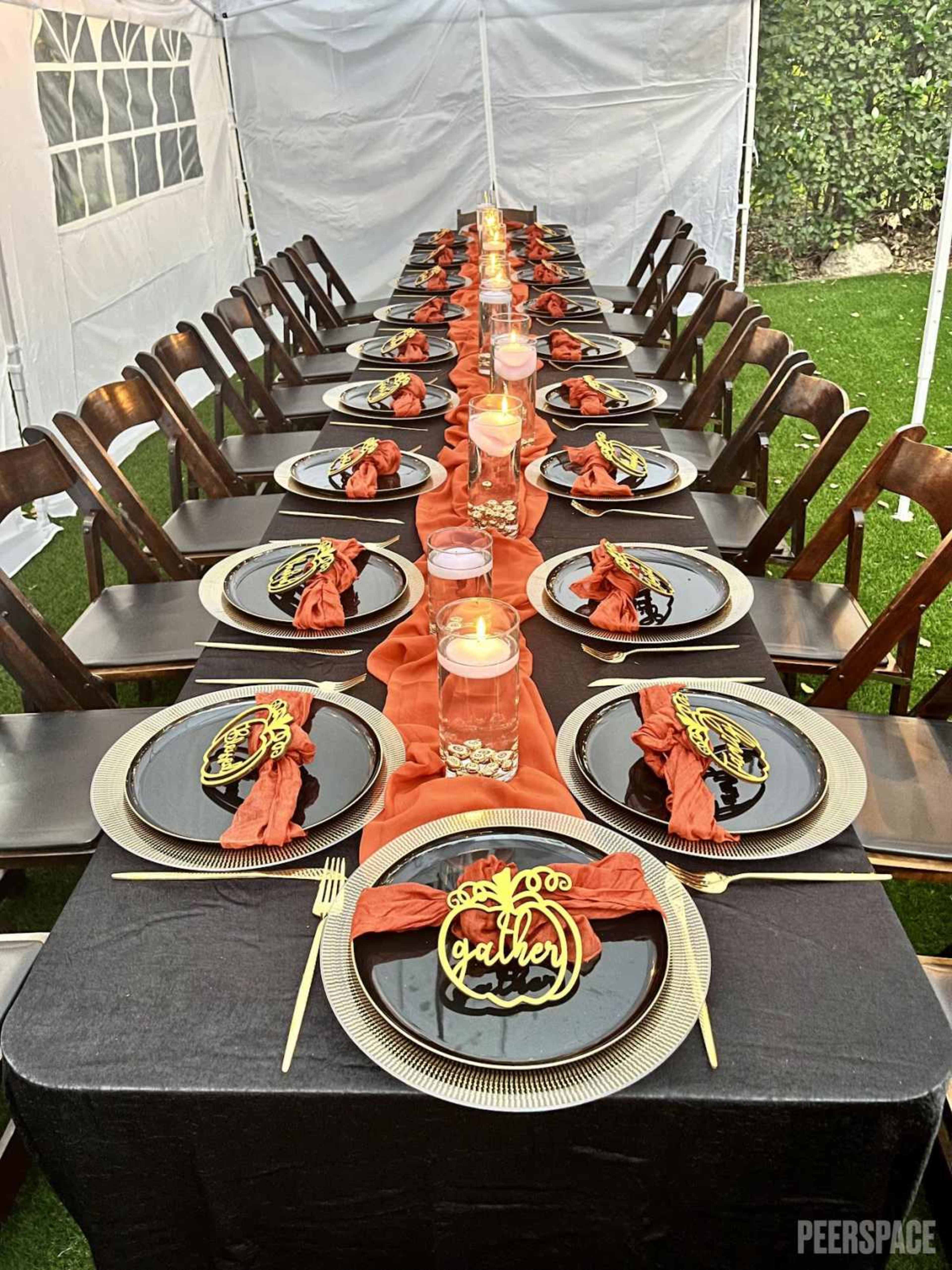 A long table is set with black plates, orange napkins, and decorative candles under a tent.