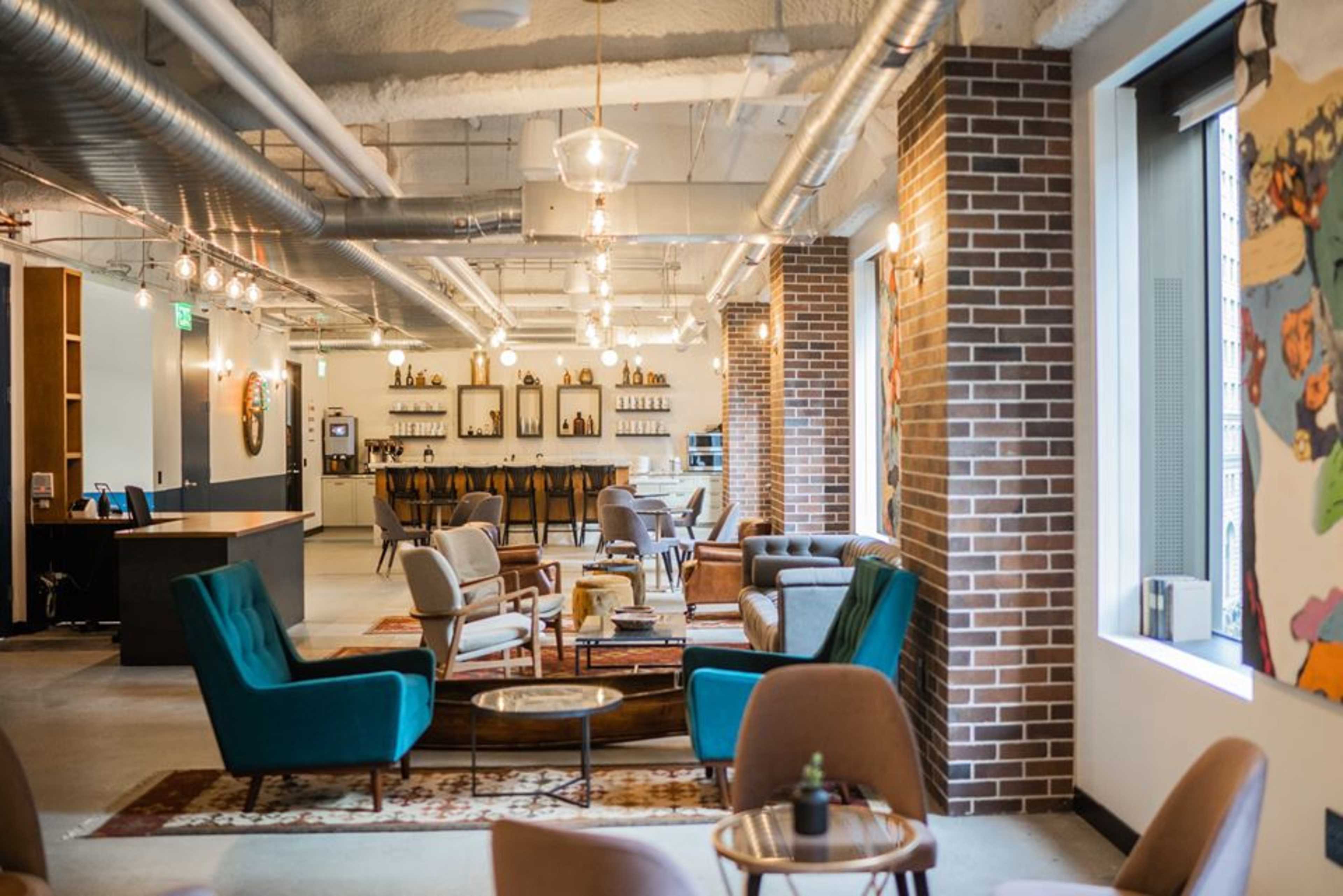 A modern office lounge area with comfortable seating, a bar in the background, and decorative lighting.