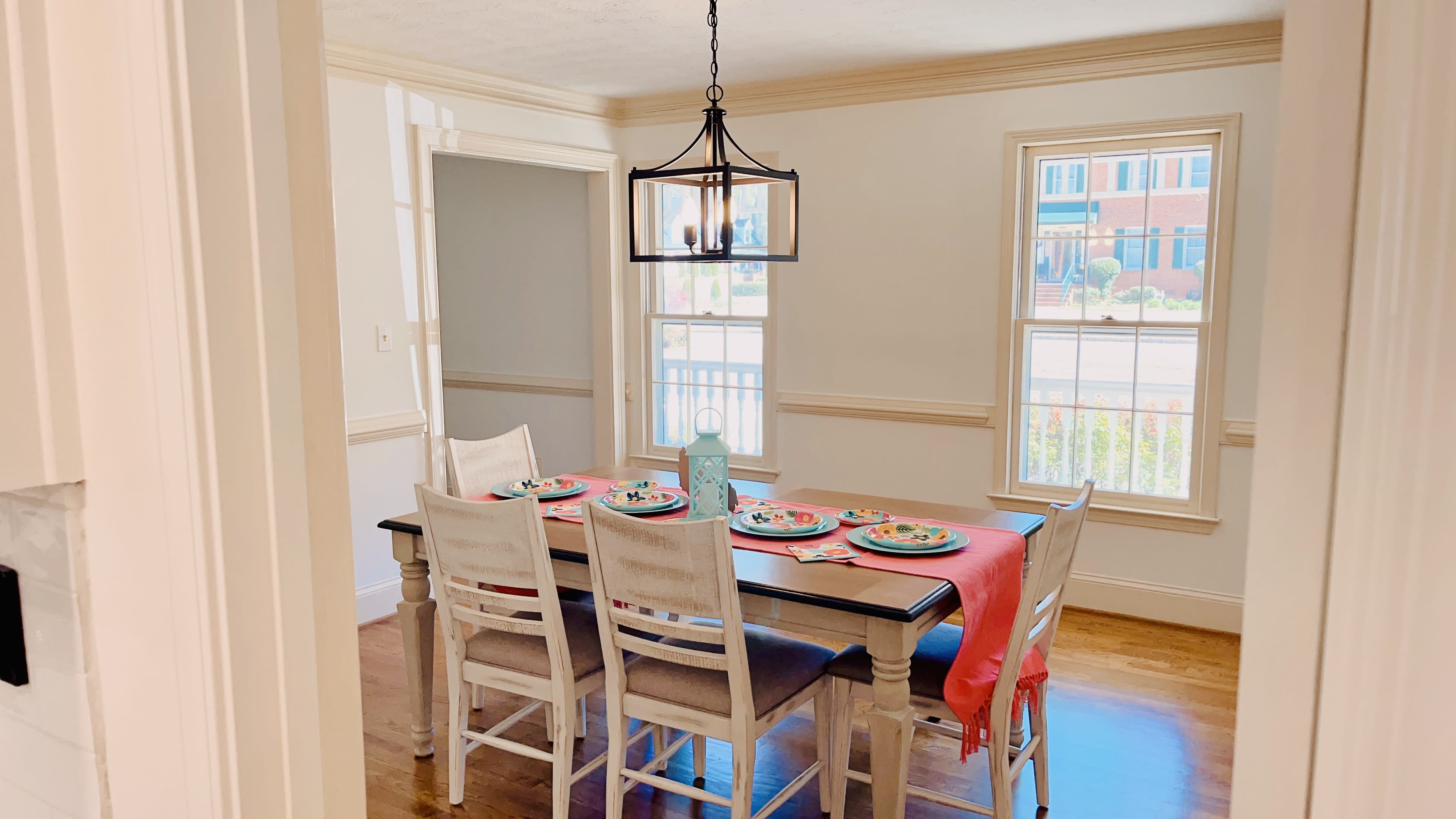 A dining room features a table set for six with plates and a pendant light hanging above.