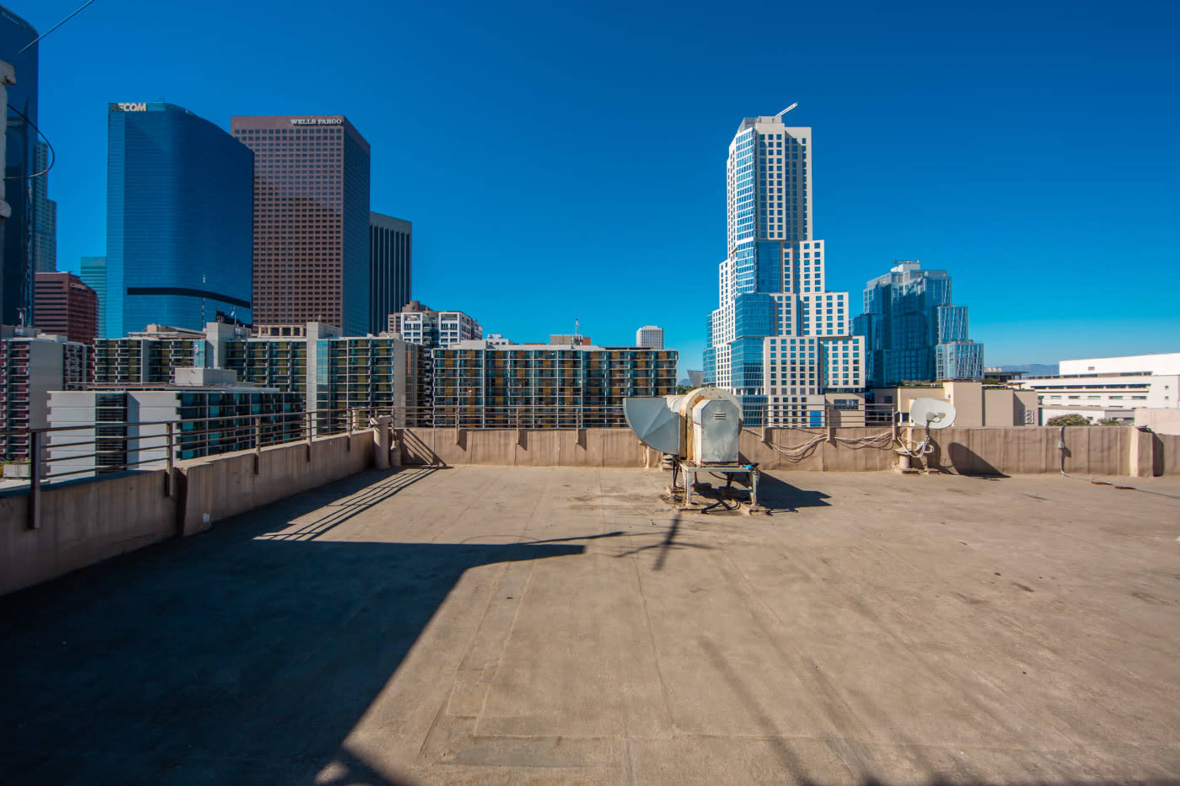 The image shows a rooftop with satellite dishes, overlooking a skyline of tall buildings against a clear blue sky.